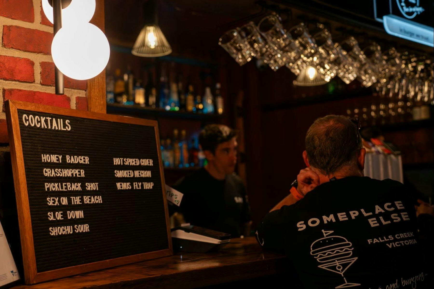 menu displayed on a board at the bar and bartender serving some visitors in the background