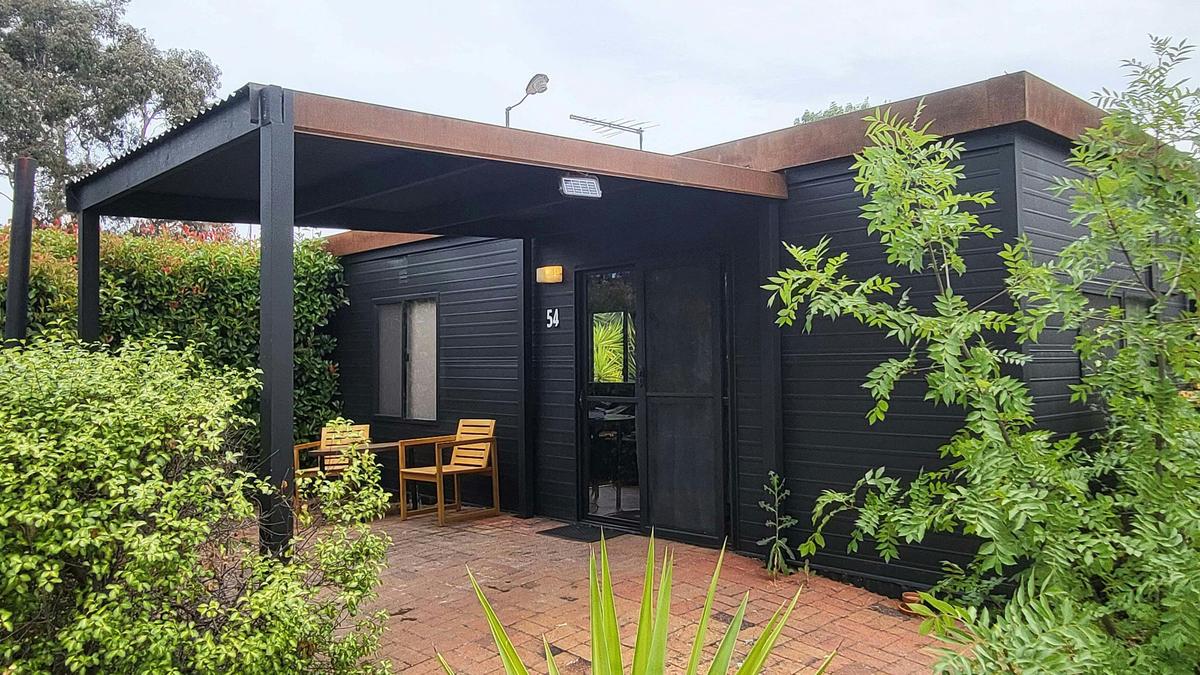 Black cabin 54 with a covered patio and wooden chairs at Stawell Grampians Gate Hotel Motel