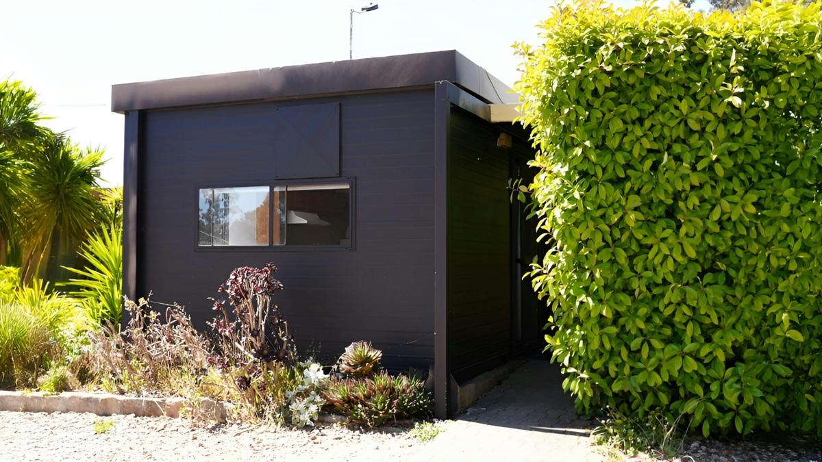 Black cabin 56 surrounded by tall greenery and garden plants at Stawell Grampians Gate Hotel Motel