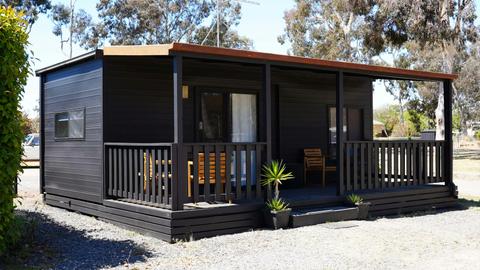 Black cabin 57 with a spacious covered porch and wooden chairs at Stawell Grampians Gate Hotel Motel