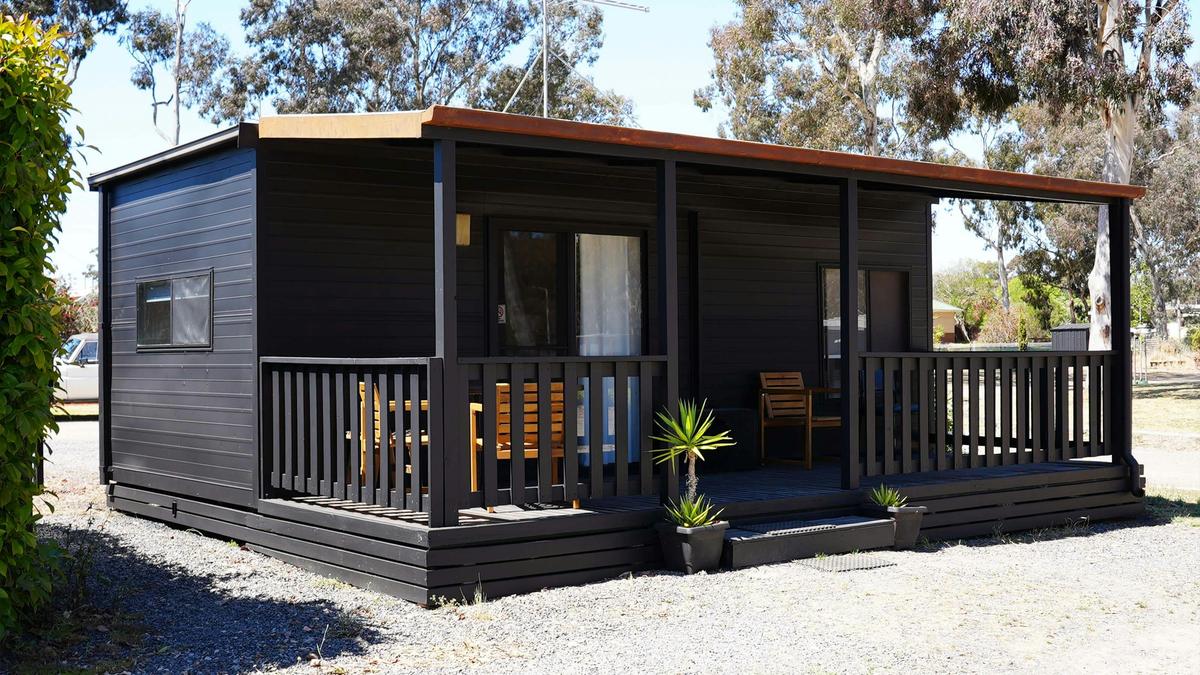 Black cabin 57 with a spacious covered porch and wooden chairs at Stawell Grampians Gate Hotel Motel