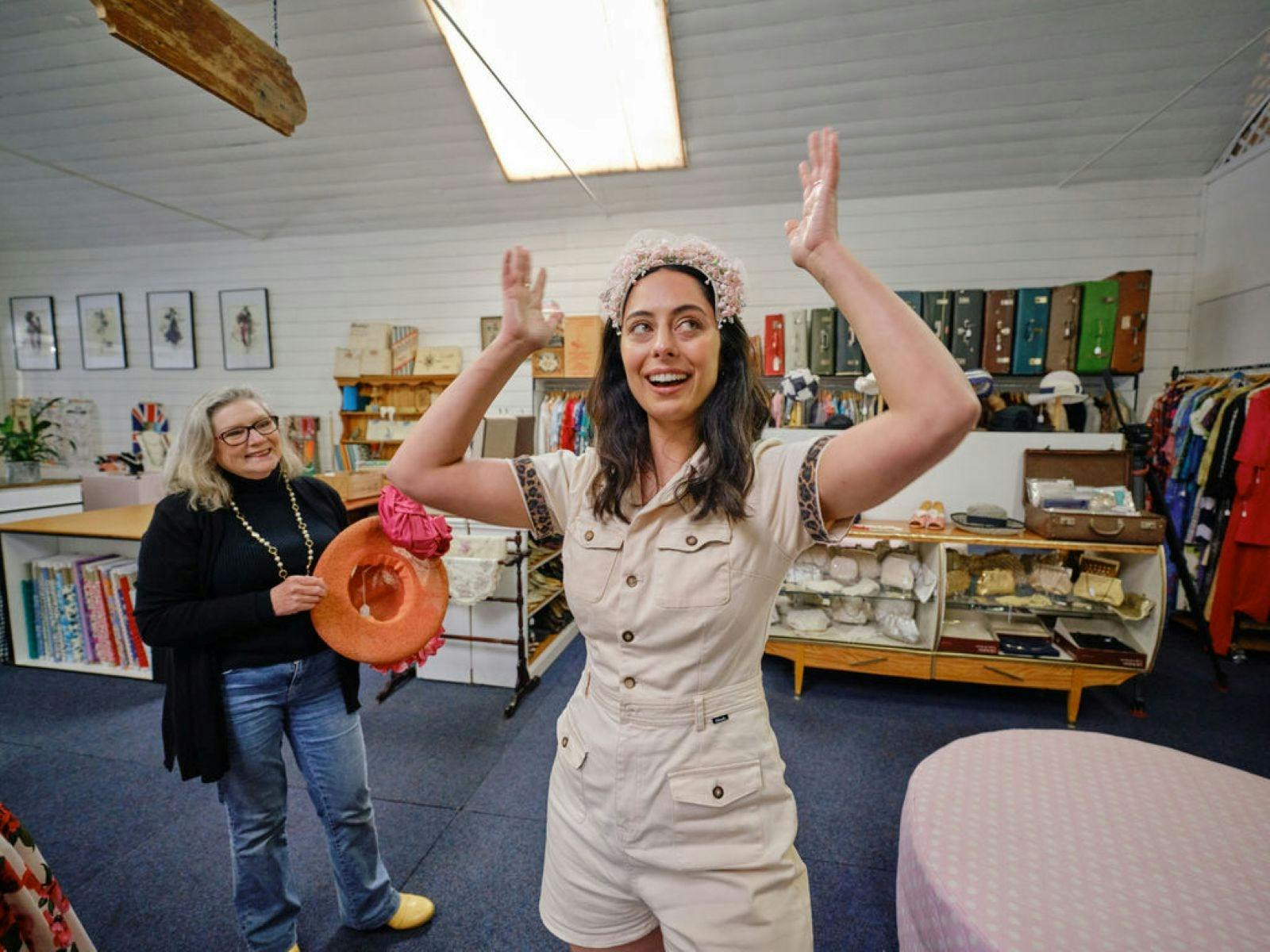 Young person trying on a vintage headpiece while shop owner looks on