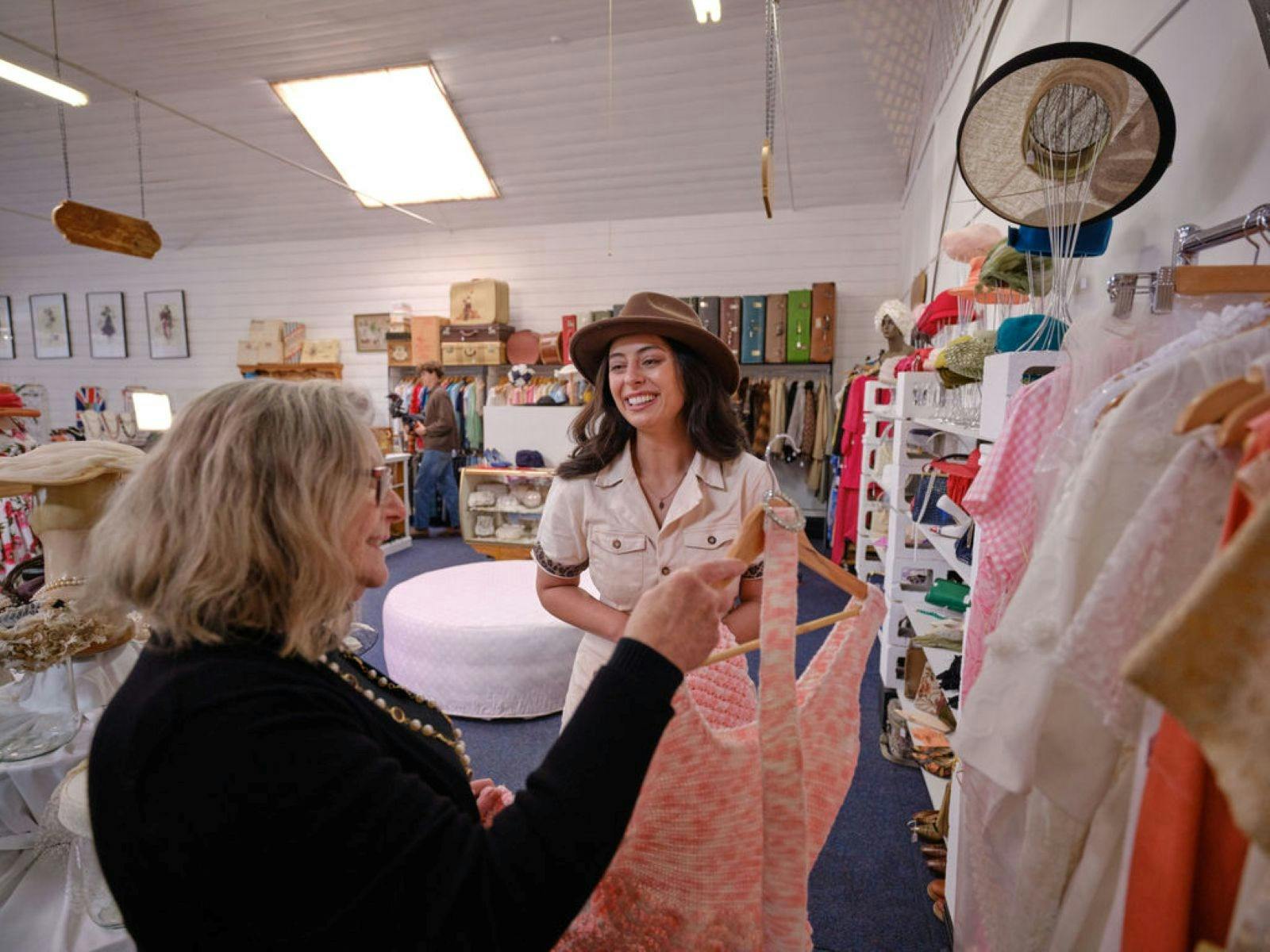 Young woman talking to owner of a shop in front of a rack of clothing
