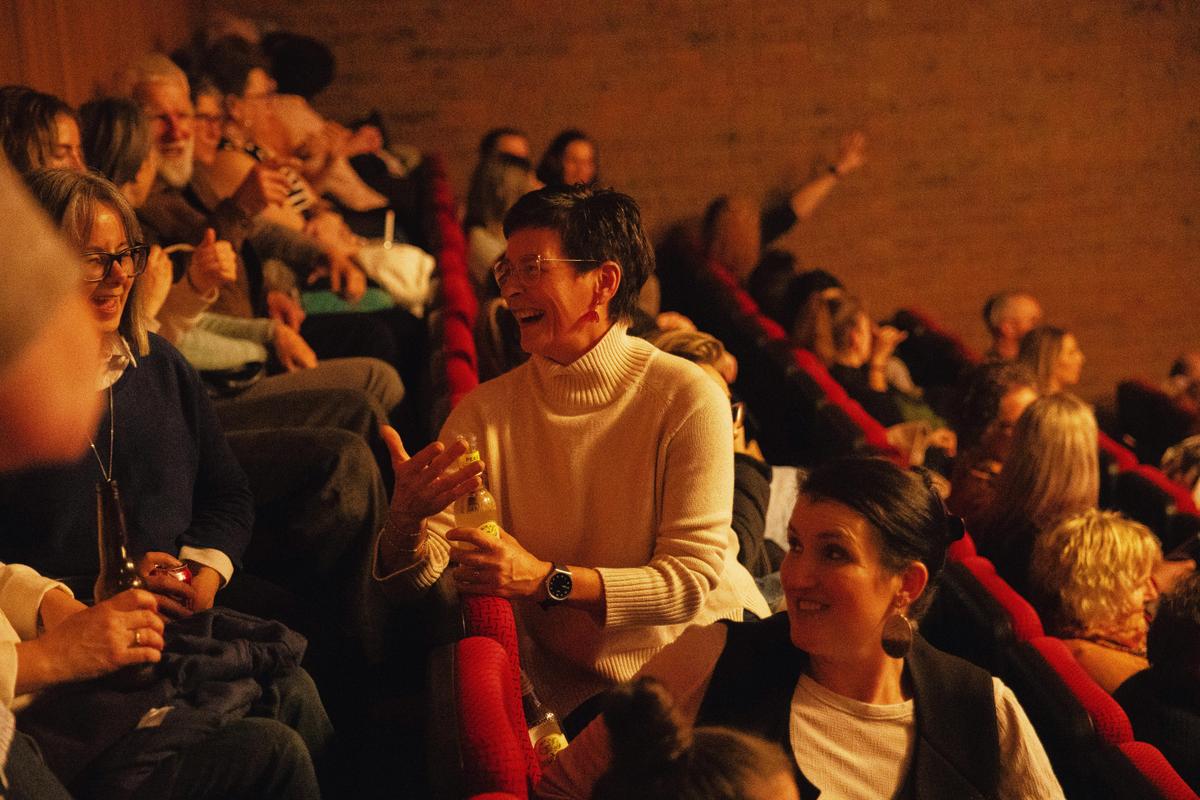 Two audience members are turning around in their seat to talk to the audience sat directly behind