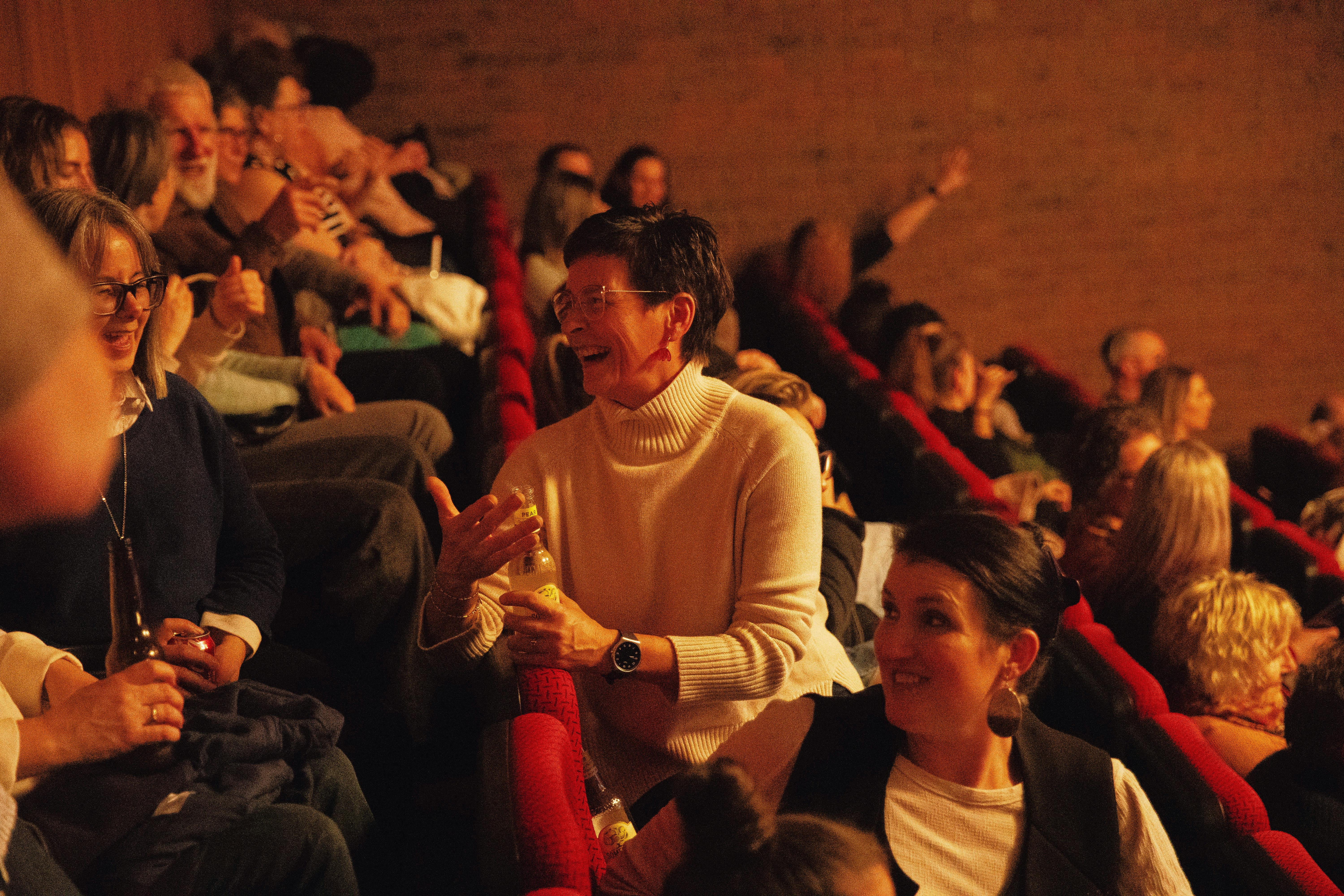 Two audience members are turning around in their seat to talk to the audience sat directly behind