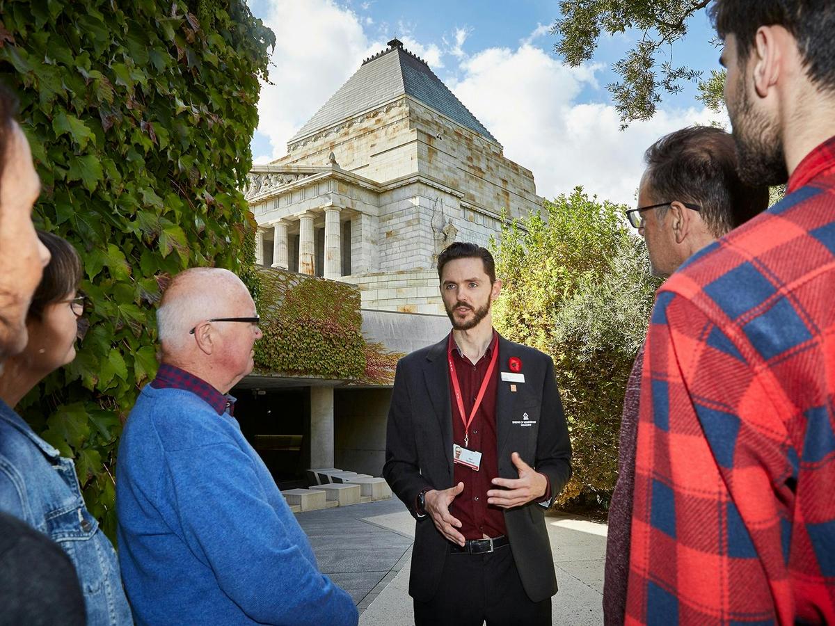 Tour Guide with tour participants stand before the Shrine of Remembrance