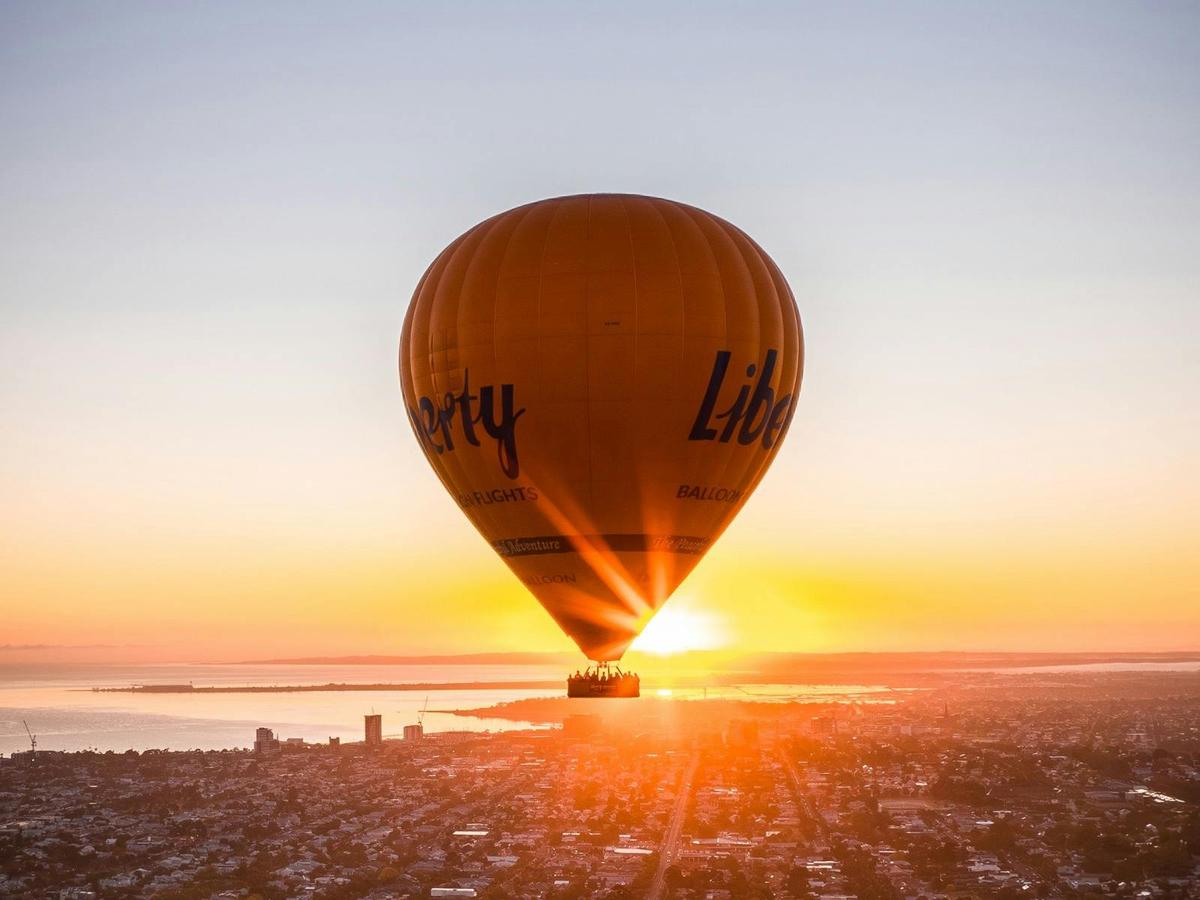 Hot air balloon adventure at sunrise, drifting above the ocean with a vibrant orange sky