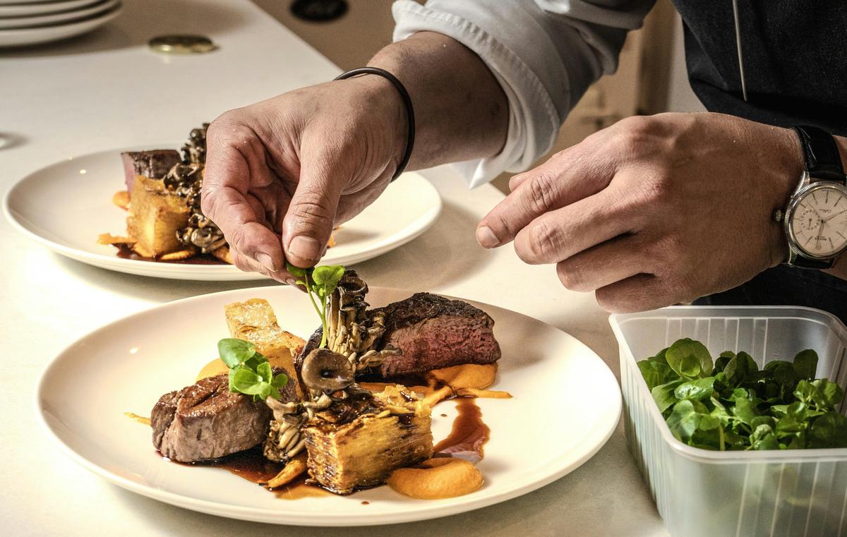 A close up of a steak dish with a chef working over it