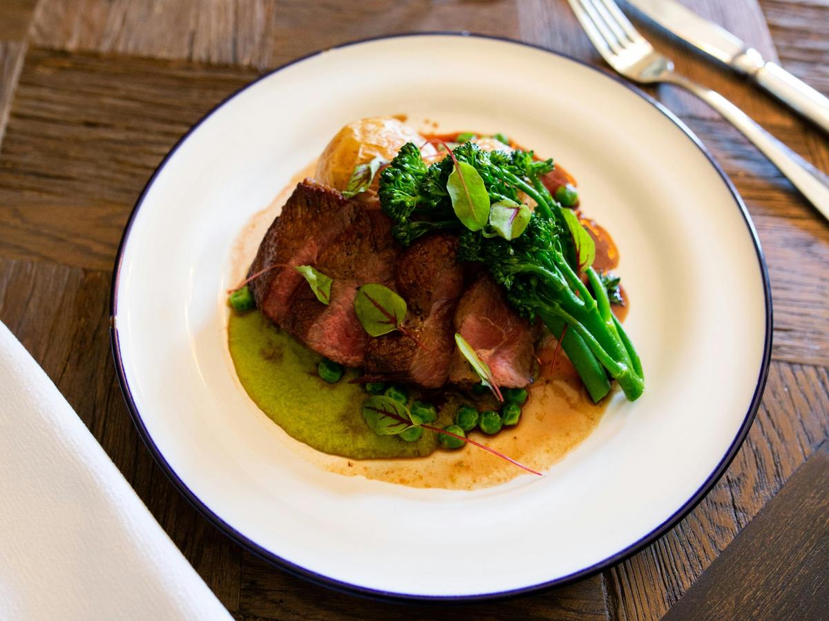 Close up image of plate of duck with broccolini dinner plate on a wooden table