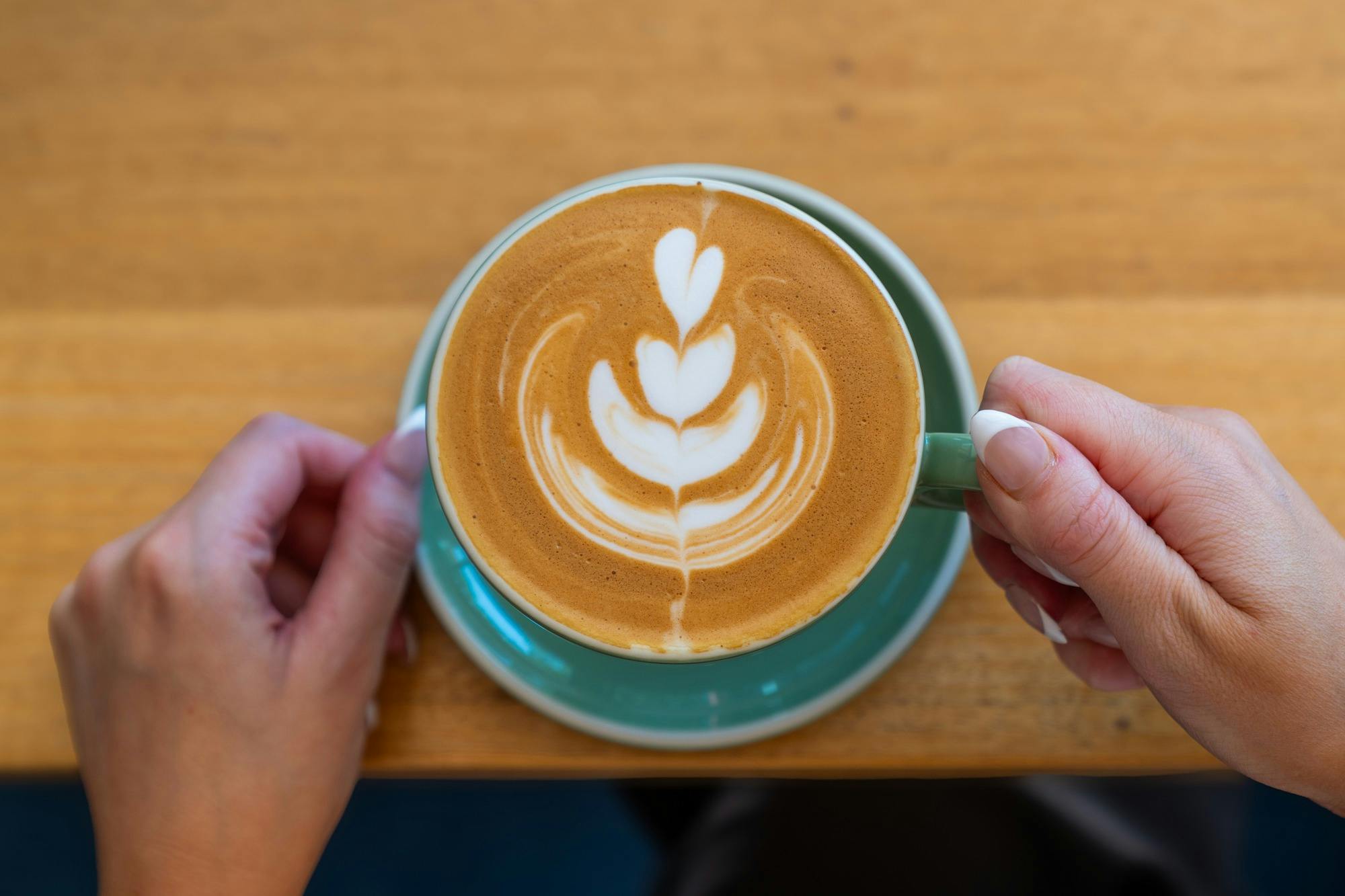 Two hands gently holding a cup of coffee with intricate latte art