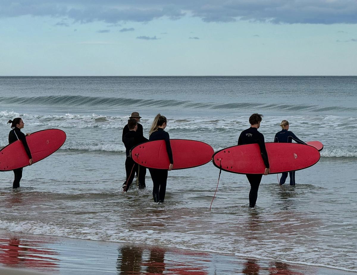 Group holding surfboards entering the ocean