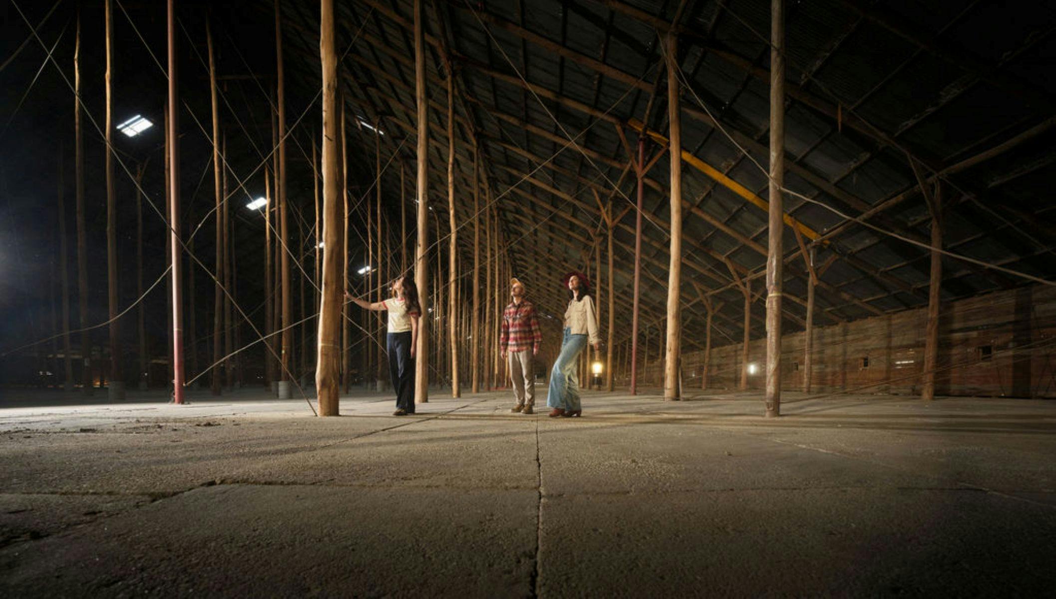three people standing in a large shed surrounded by huge pillars and looking up