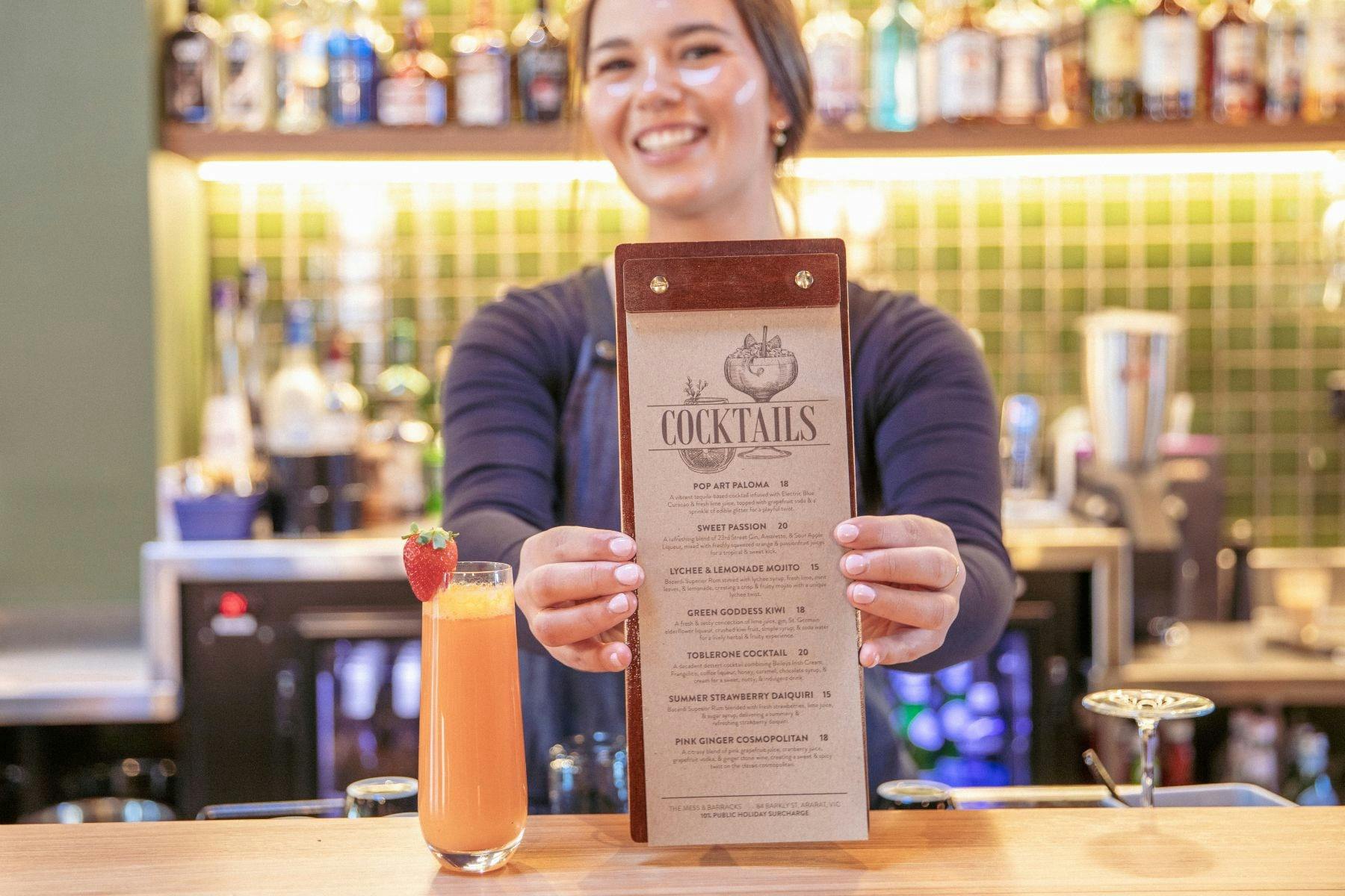 Young person holding forward a cocktail menu from behind a bar