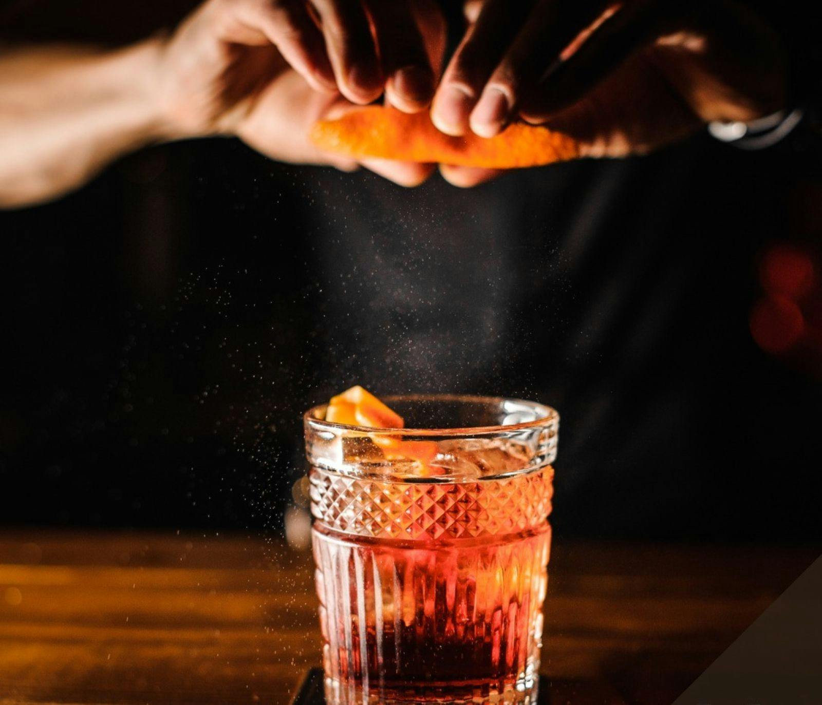 Two hands zesting an orange peel into a glass