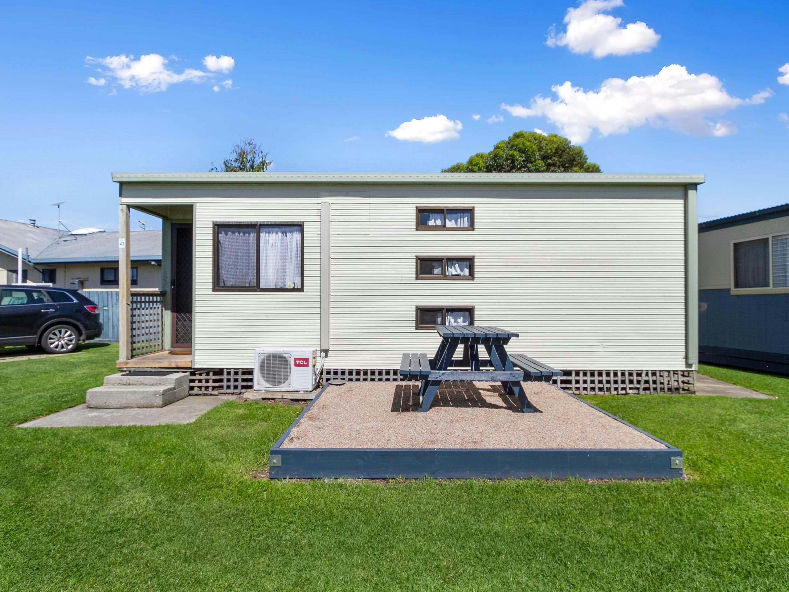 Neat cabin with picnic table out front. The cabin is surrounded by lush green grass.