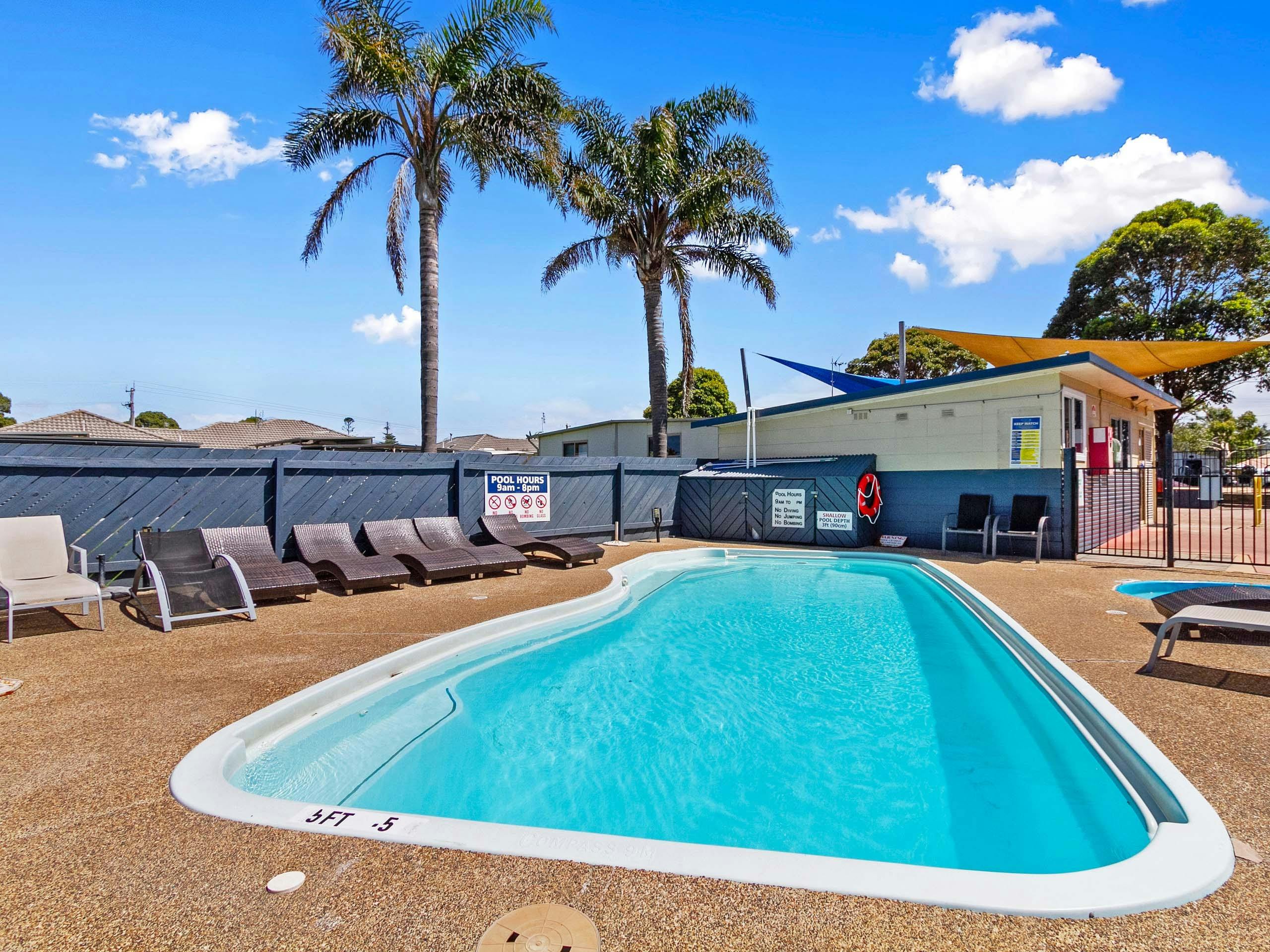 Sparkling blue swimming pool, with Palm Trees in the background and sun lounges in the foreground.