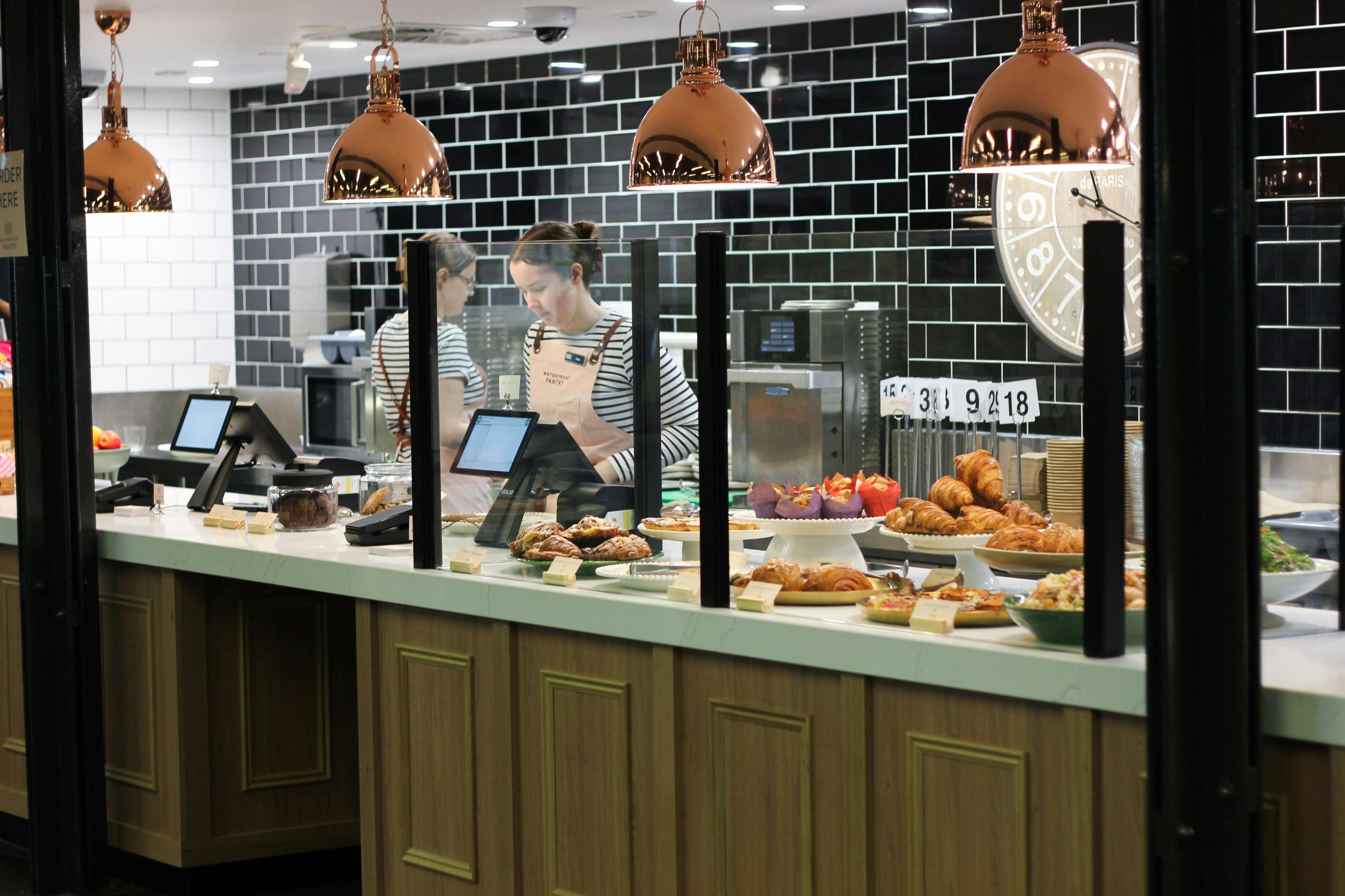 Two staff members working behind a counter with lots of pastries and food displayed on platters
