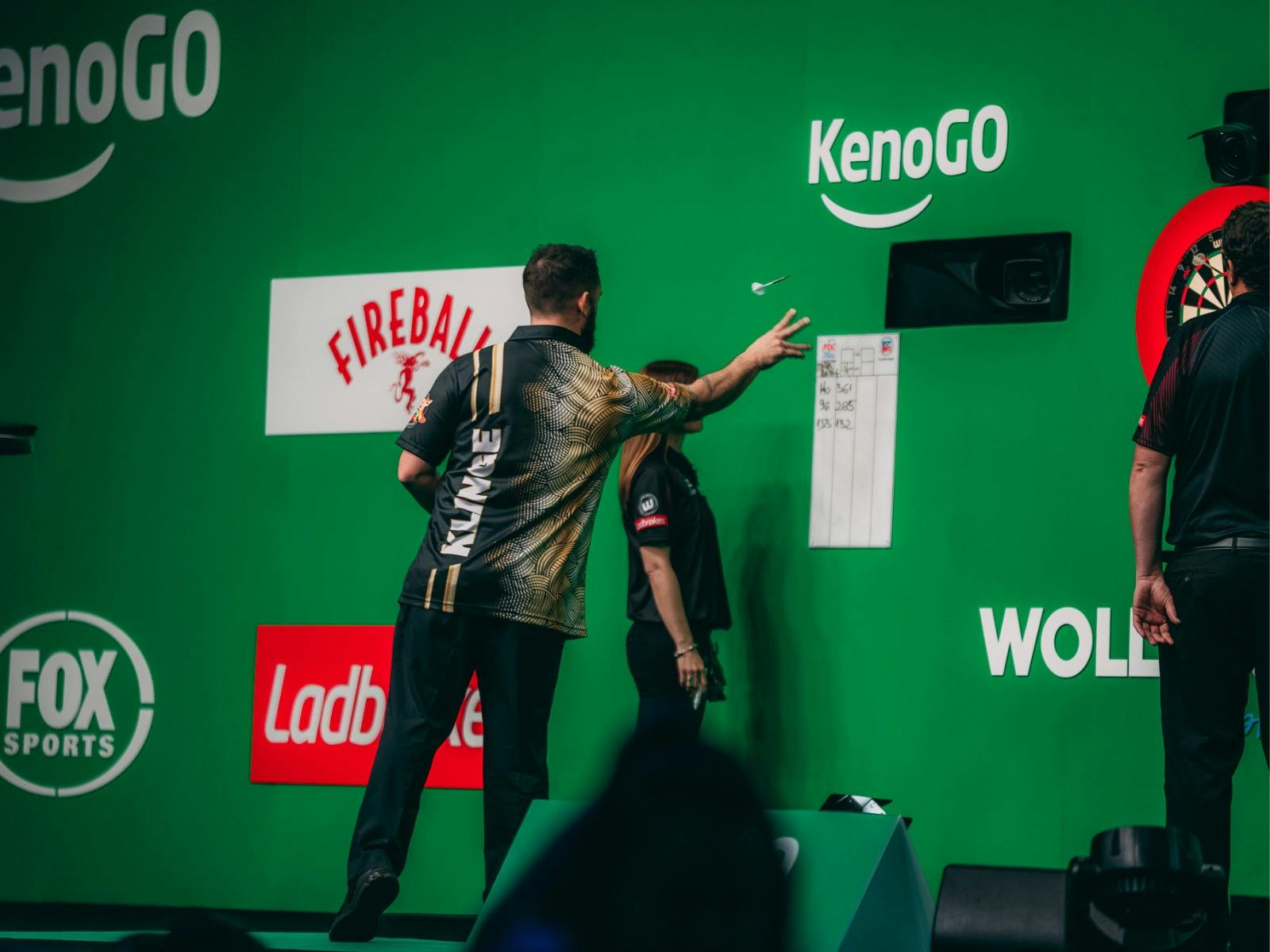 Darts player taking their turn, throwing dart at target.