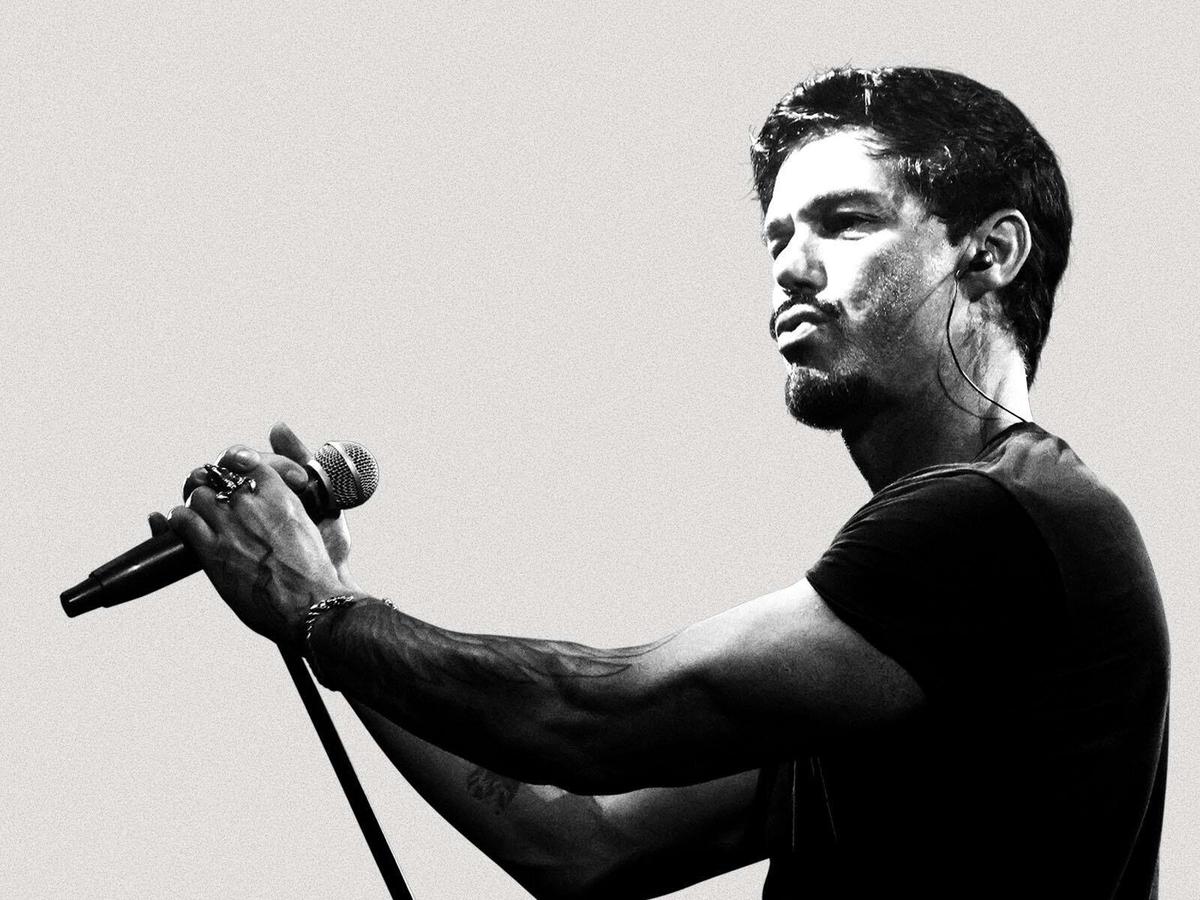 A man with a black t-shirt standing holding a microphone, looking to the left of camera