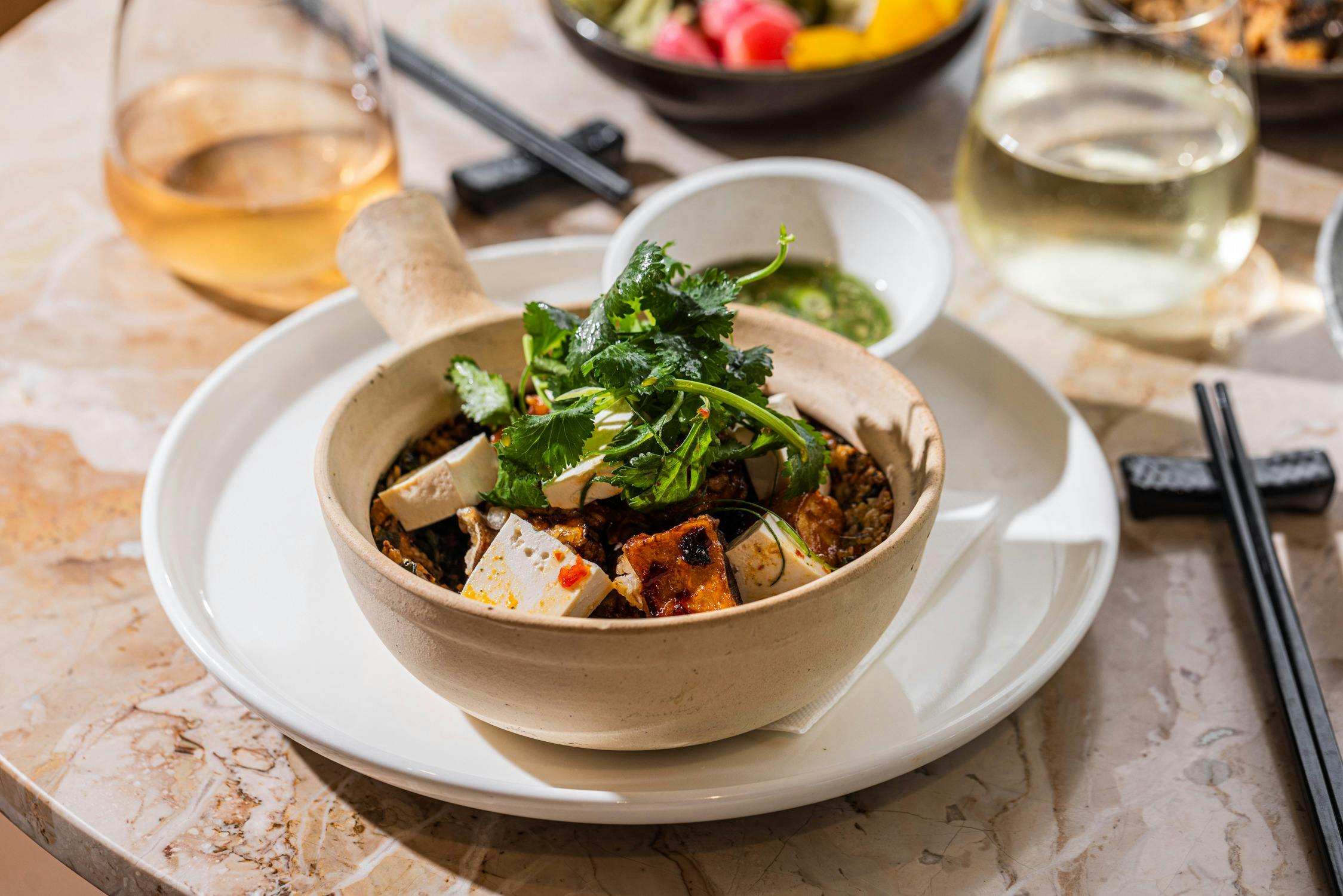 an asian tofu curry with coriander on a table with a glass of white wine