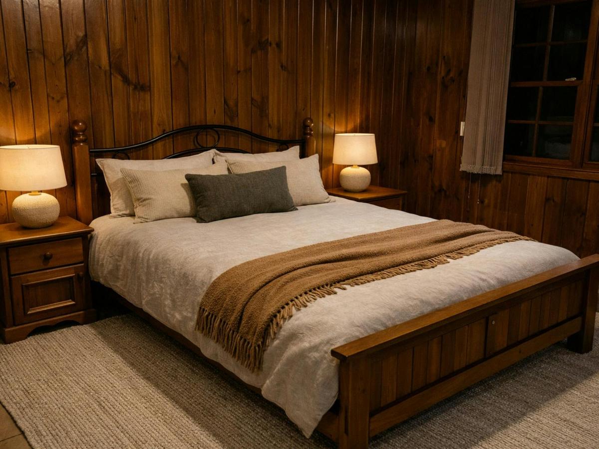 Warm timber bedroom with a beautifully made bed and soft bedside lighting