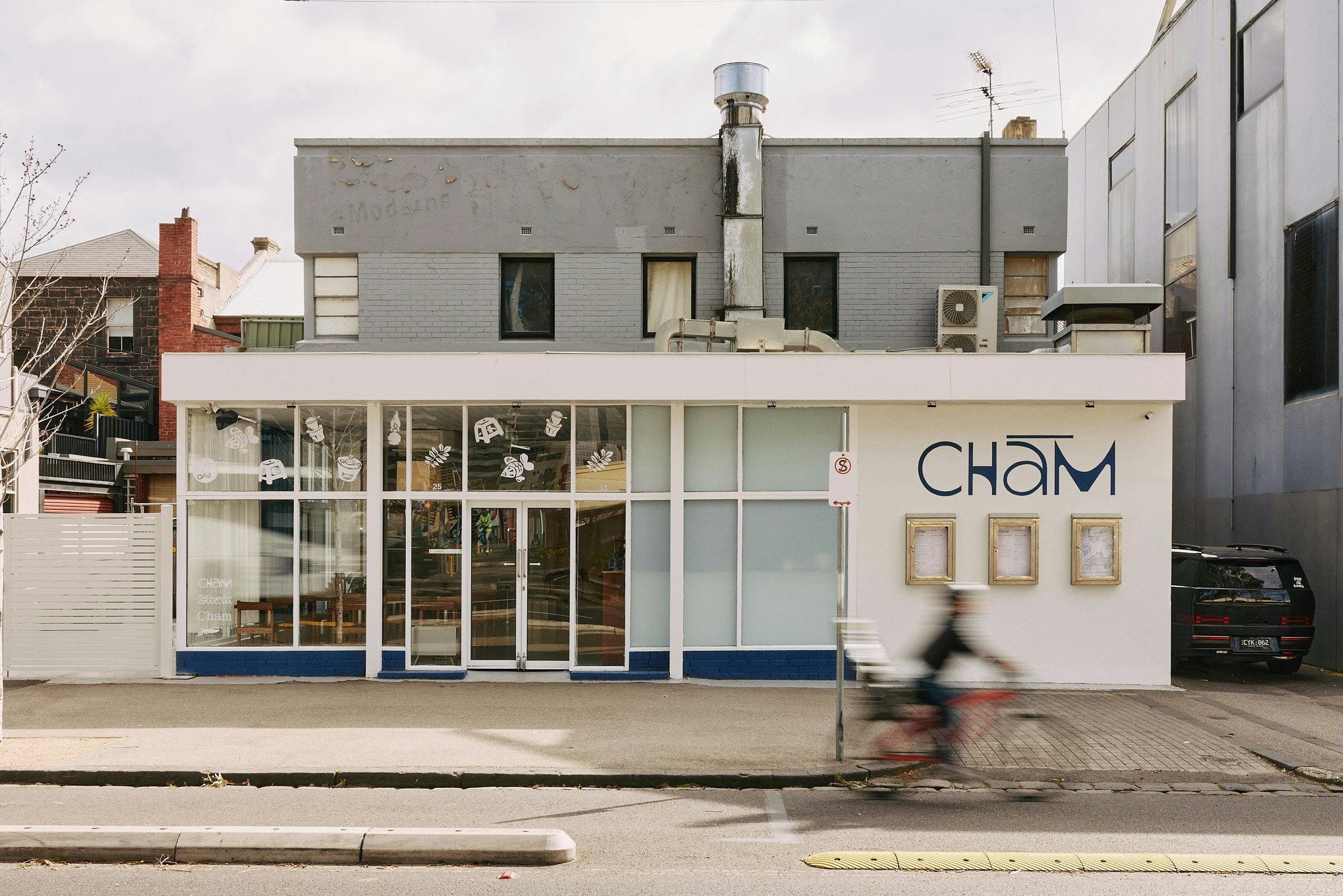 A bright white façade with indigo accents and large windows opening into Cham.
