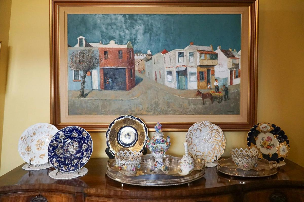 Painting sits atop an antique chest of drawers with decorative plates on top