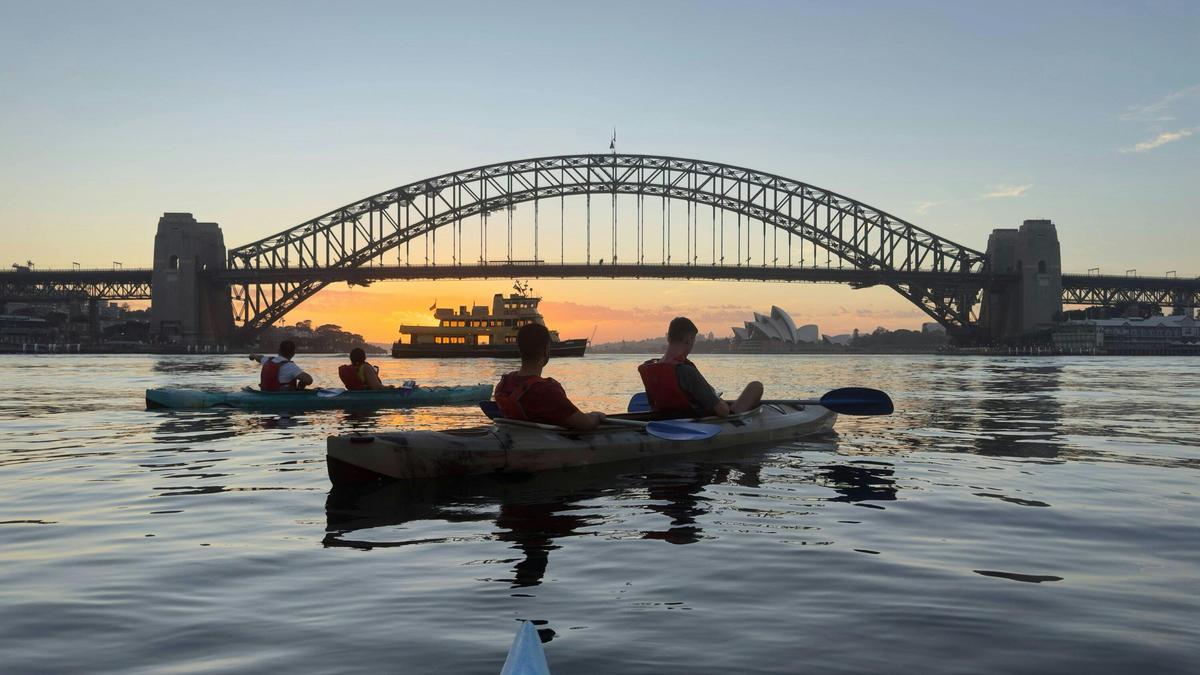 Double kayak passing beneath Sydney Harbour Bridge as the sun rises over the harbour