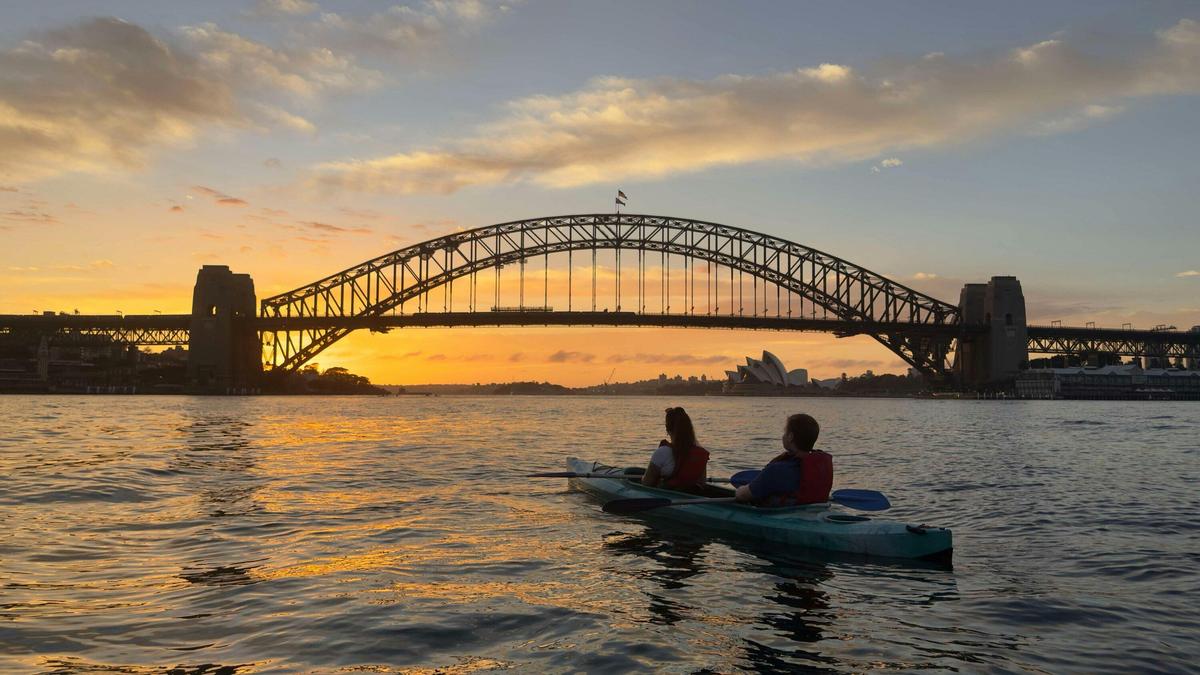 Sunrise kayak tour passing under Sydney Harbour Bridge at golden hour