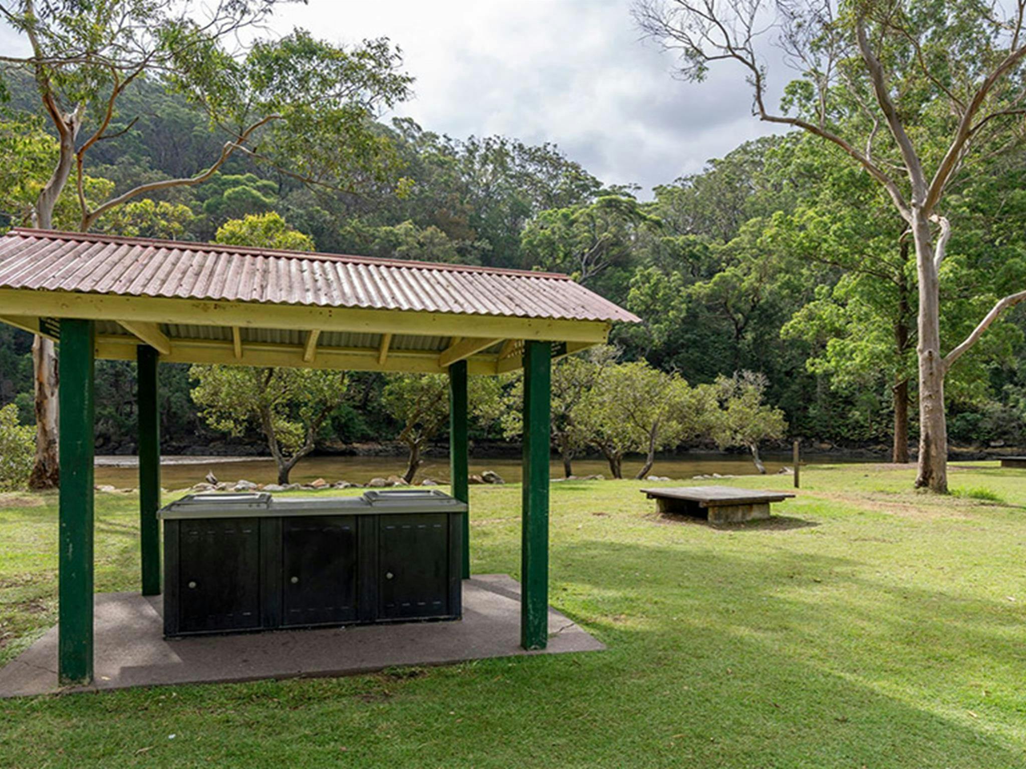 Sheltered barbecues next to a picnic platform on a lawn at Apple Tree picnic area with a creek and