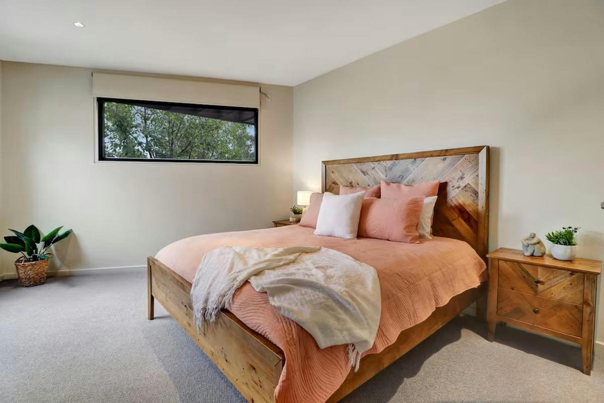 Calm and comfortable main bedroom with timber bed, soft styling and natural light at Banksia House H