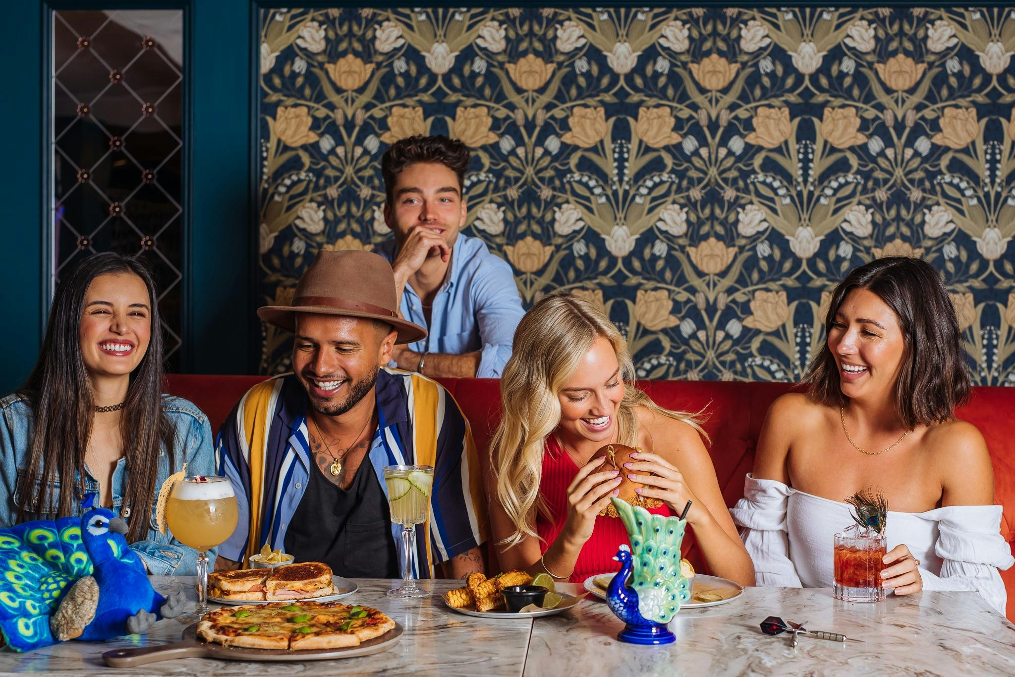 Group of five men and women eat burgers and drink cocktails together laughing