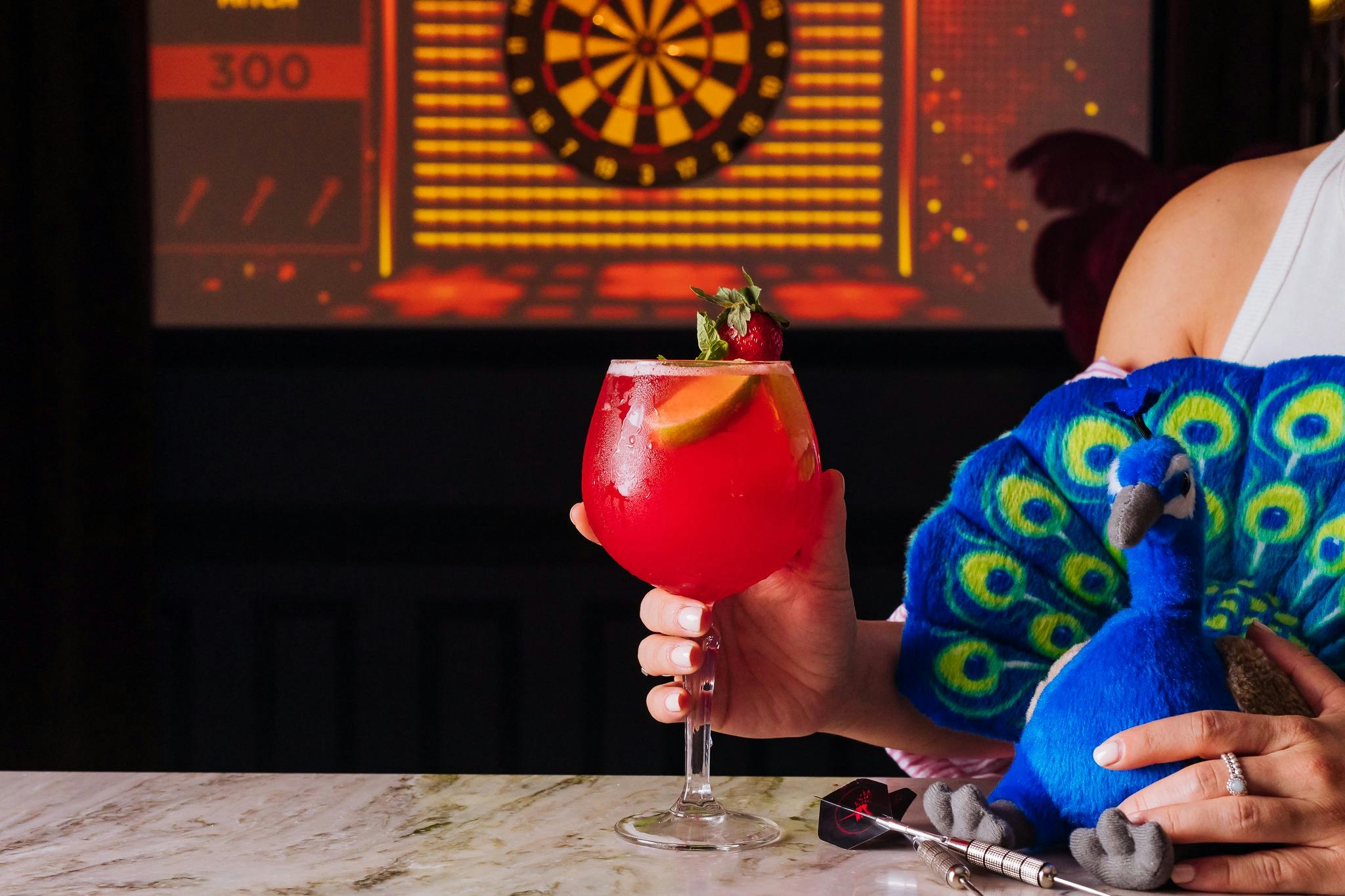 Red cocktail on table with peacock plush sitting next to it.