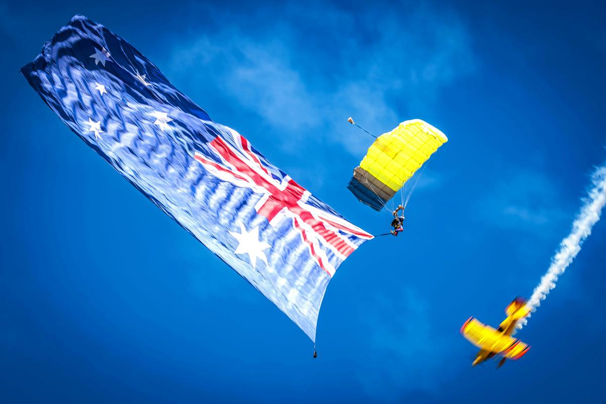 A skydiver carrying an Australian flag descends as the Wolf Pitts Pro flies past