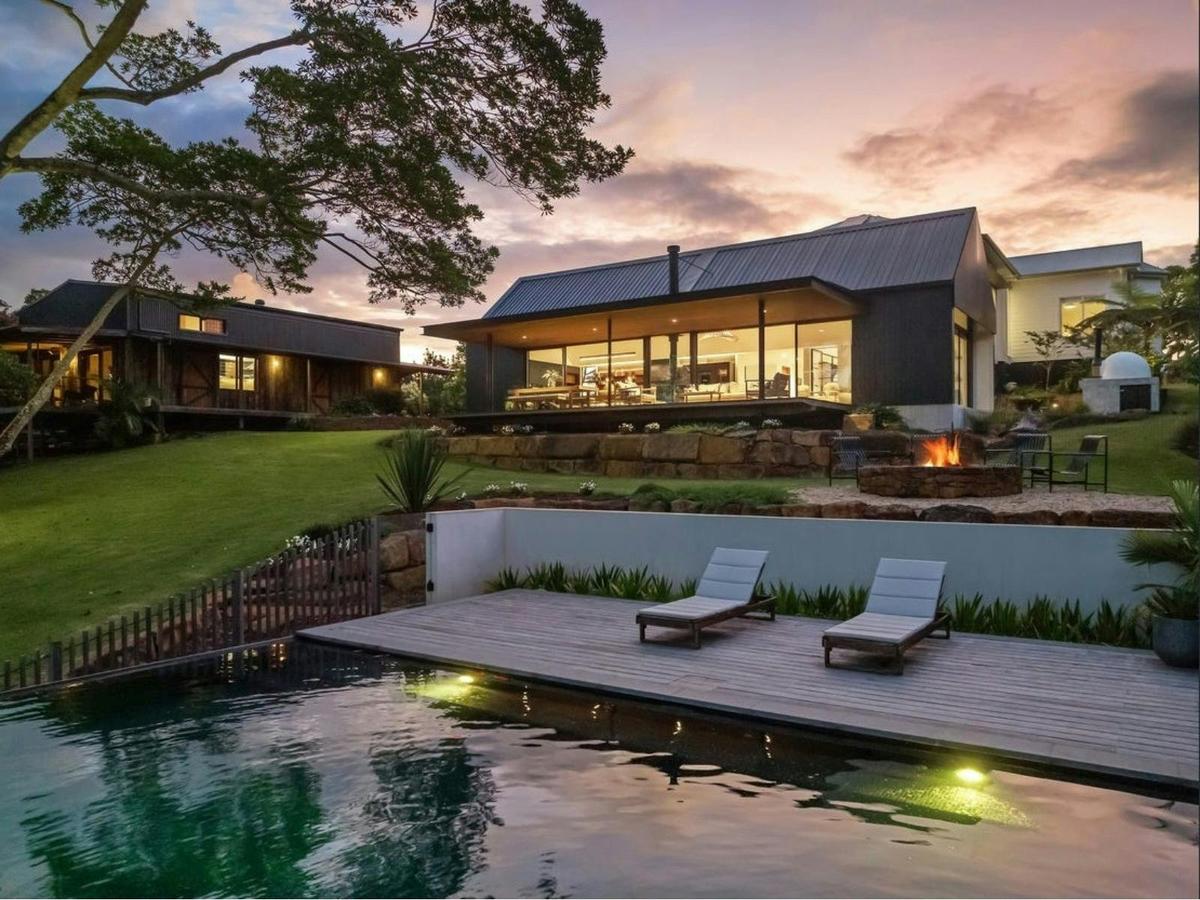 Infinity pool, fire pit and contemporary pavilion at dusk.