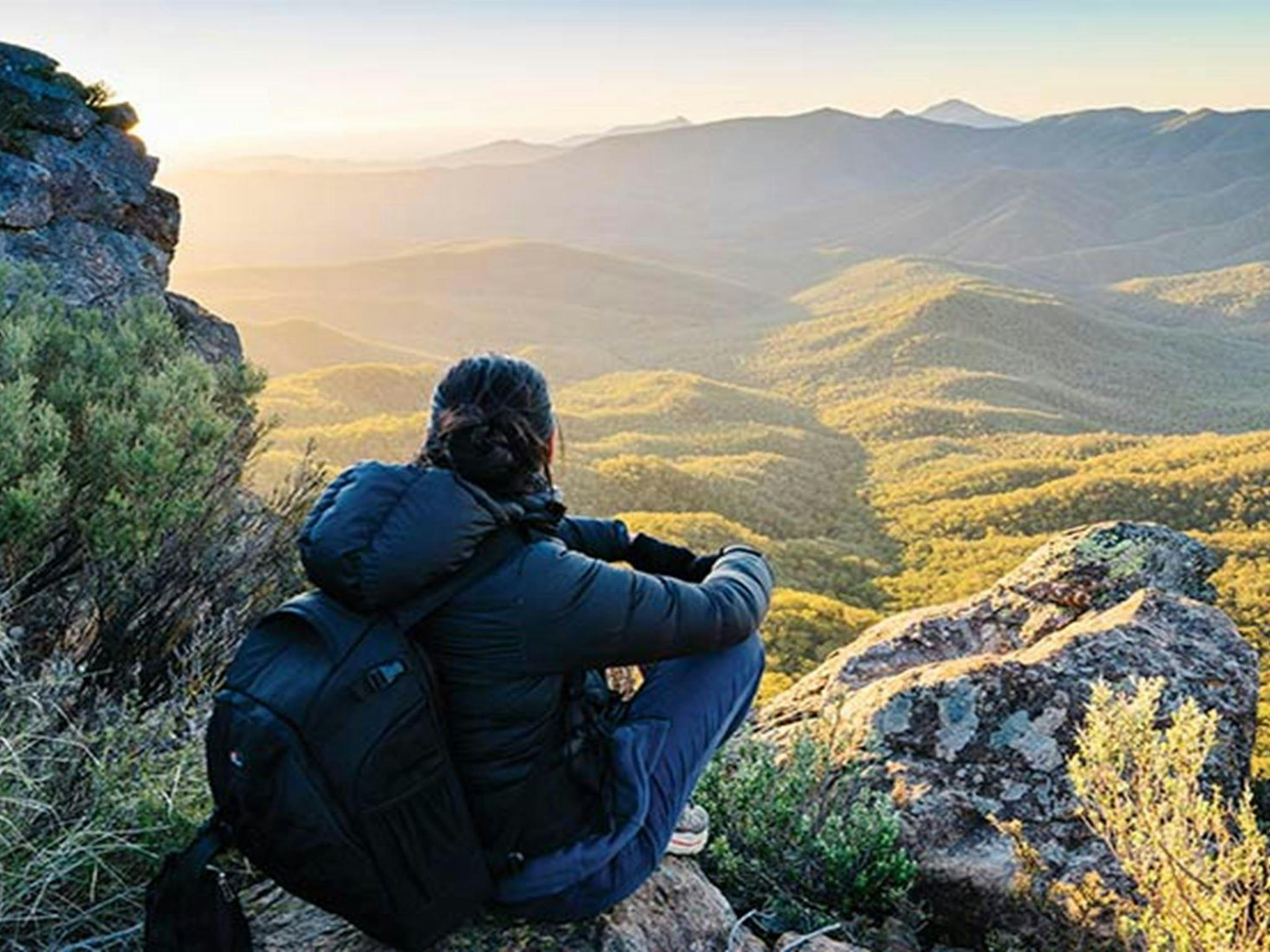 Woman crouching on rock enjoying sunset views from The Governor lookout walking track. Photo: Simone
