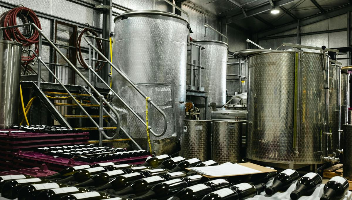 Winery interior featuring stainless steel tanks and bottles in pink storage trays.