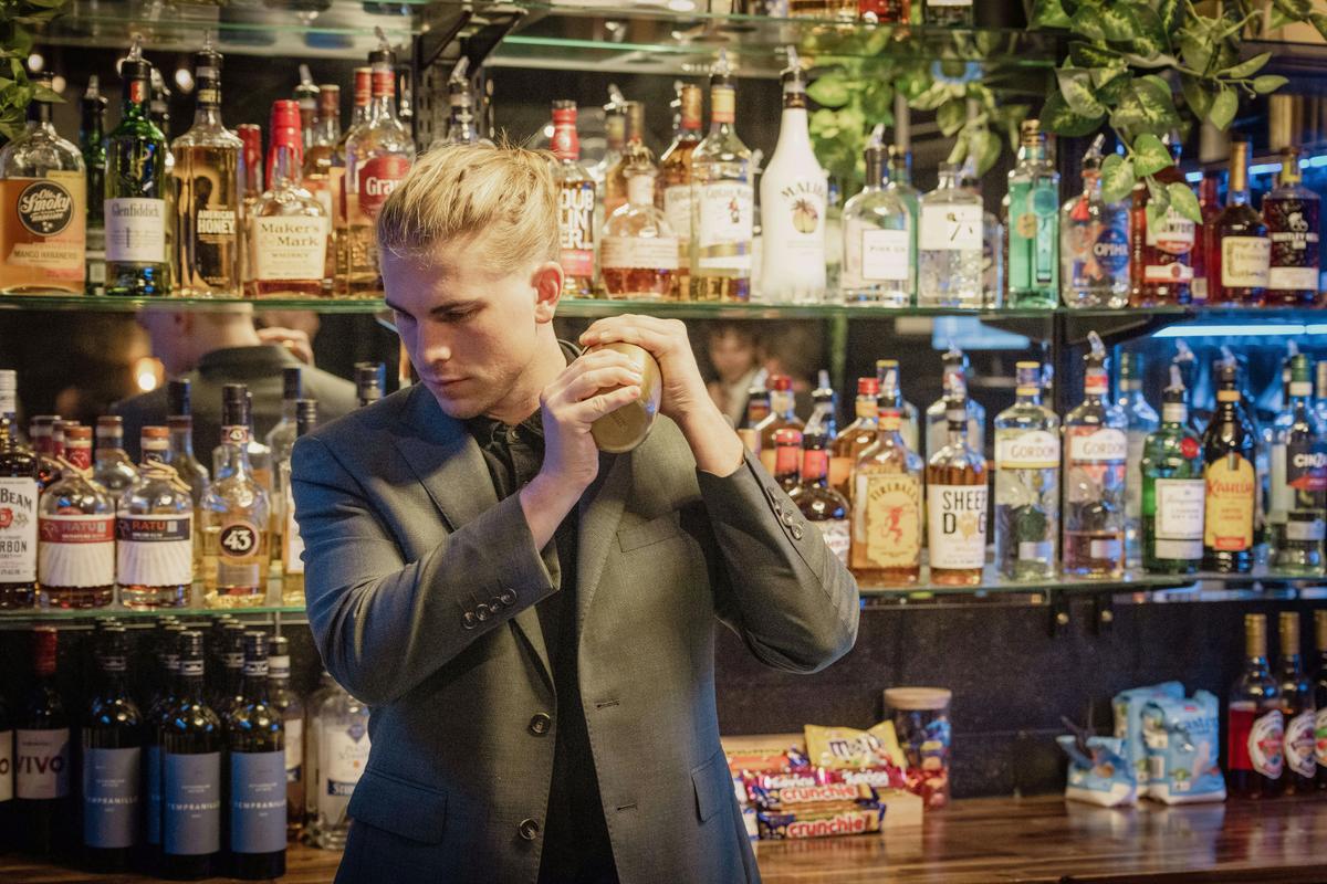 Man in a green suit shaking a cocktail behind a bar