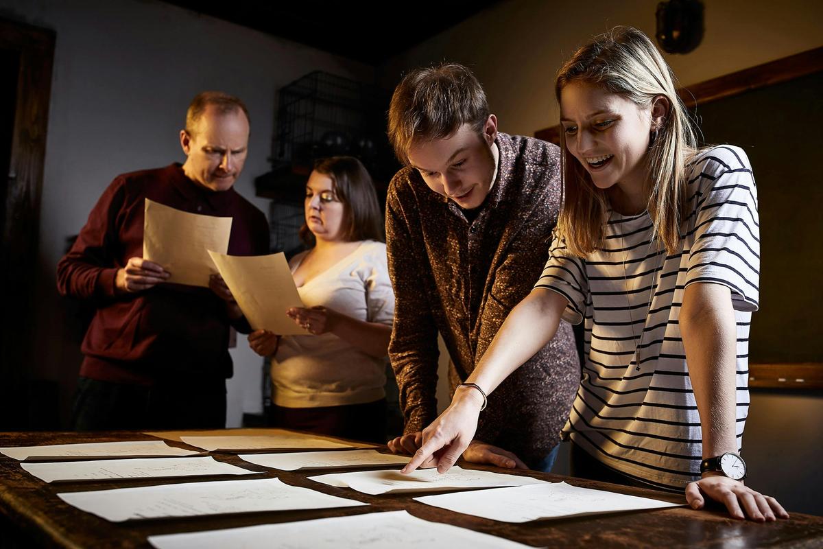 4 people pointing at clues on a table and smiling