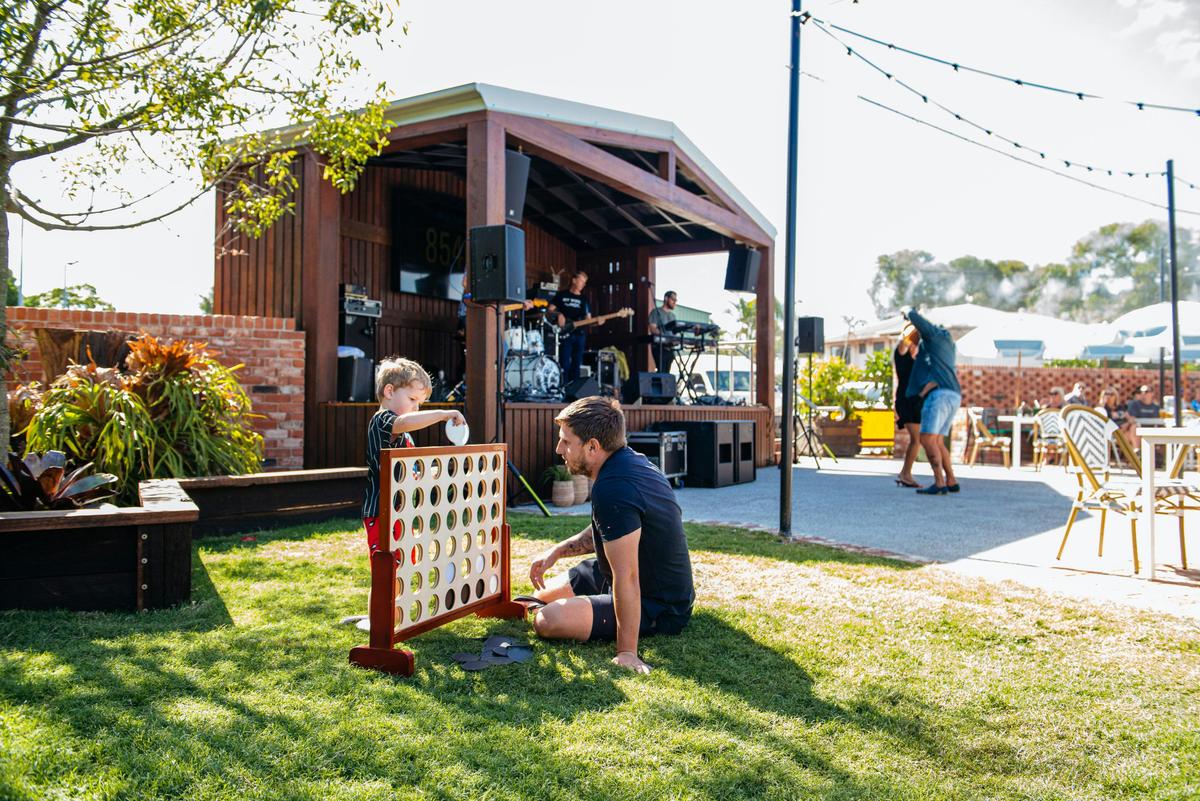 A young boy and a man play a game on a sunny lawn while a live band performs on stage