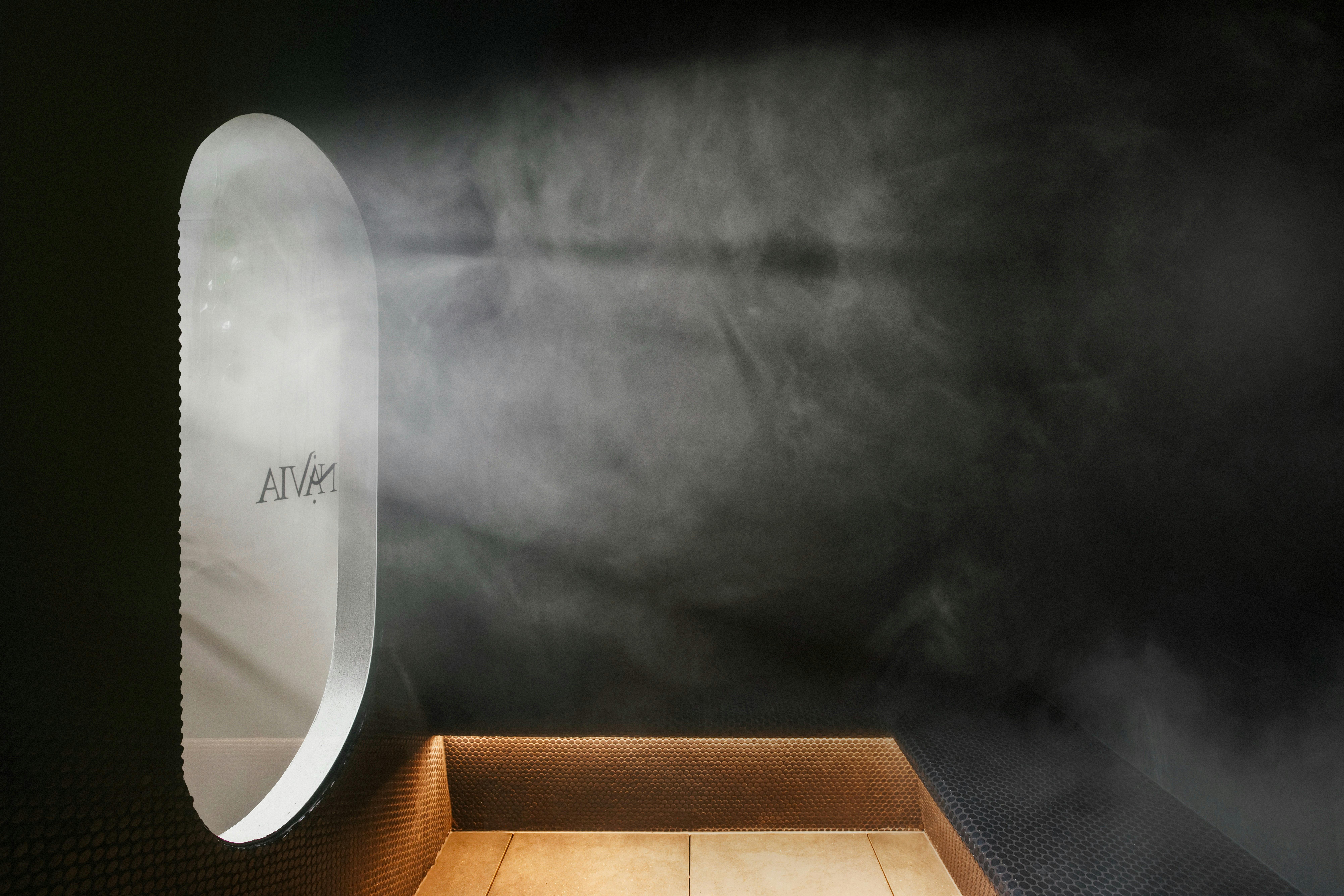 Light coming through a rounded window with the Navia logo, illuminating steam in a steam room.