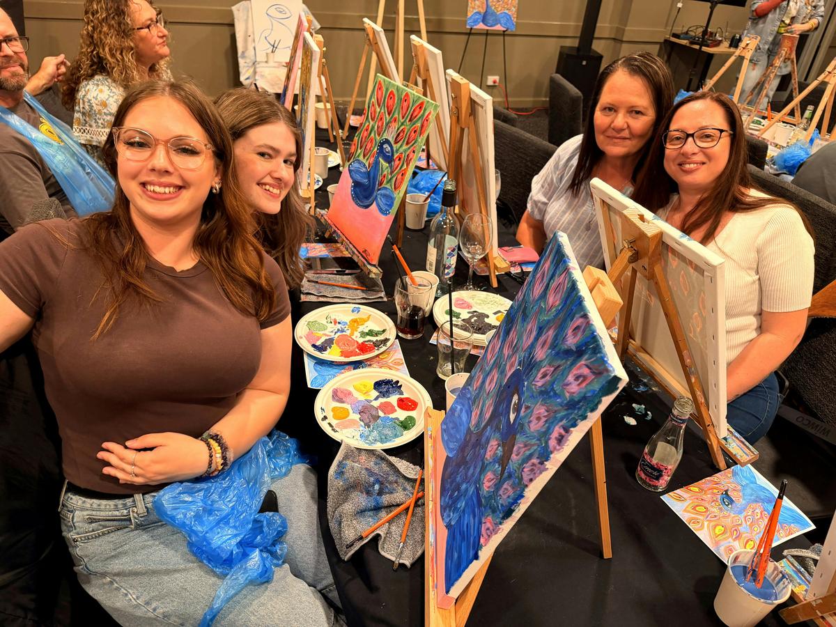 Group of Paint Juicy guests holding their finished peacock paintings at a mobile paint and sip event