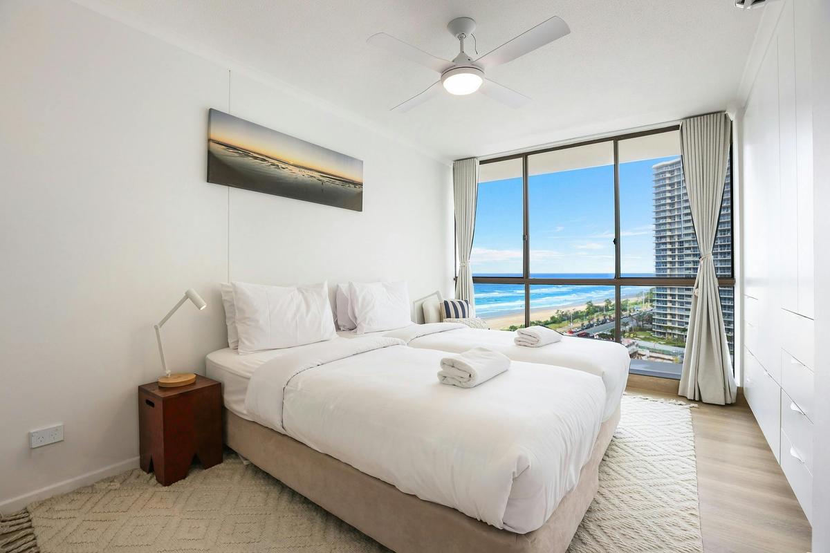 Second bedroom with 2 single beds with floor to ceiling windows on the left side with ocean/ city