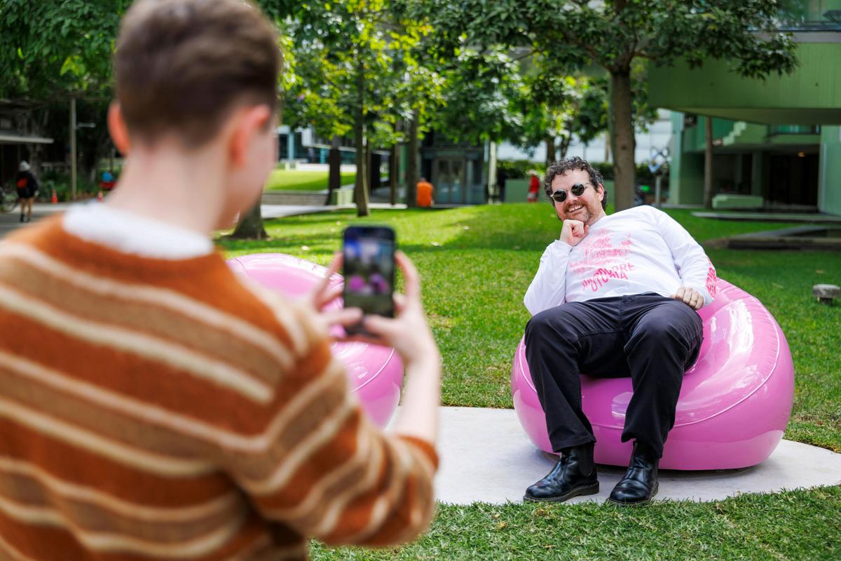 Man posing for a photo on a solid pink chair that looks like its inflatable