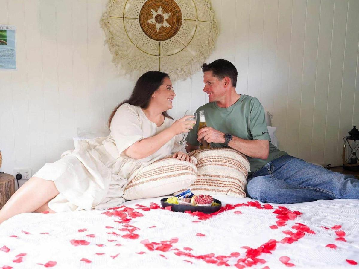 Couple relaxing and sipping wine with rose pellets all round them, and our tablelands cheese platter