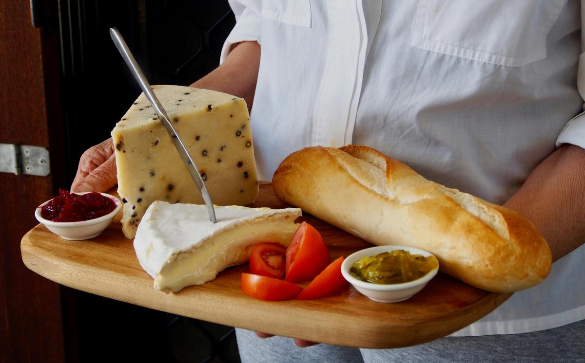 A close up image of a cheese platter with olives, cut up tomatoes, bread loaf, chutneys