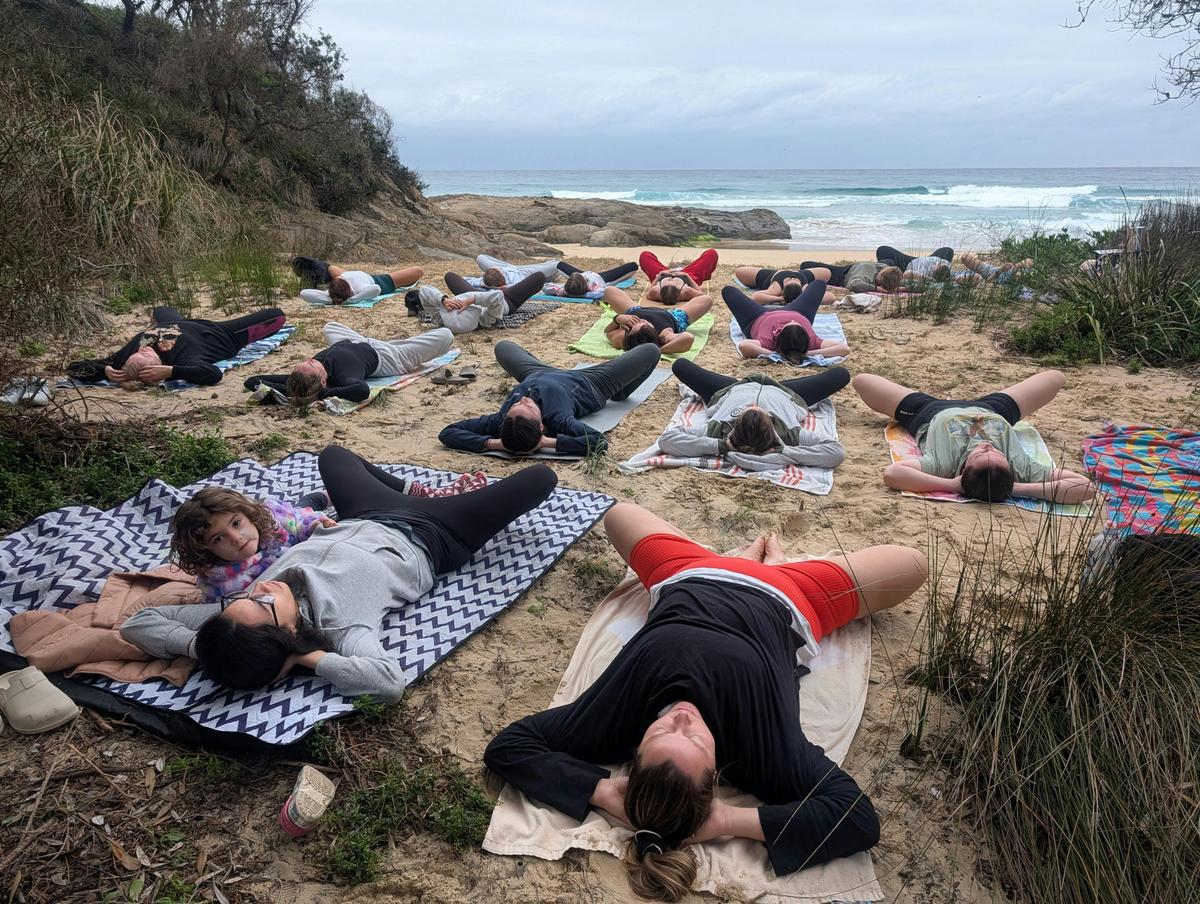 A group of students, including children,  lying in yoga poses, embracing some ocean wellness