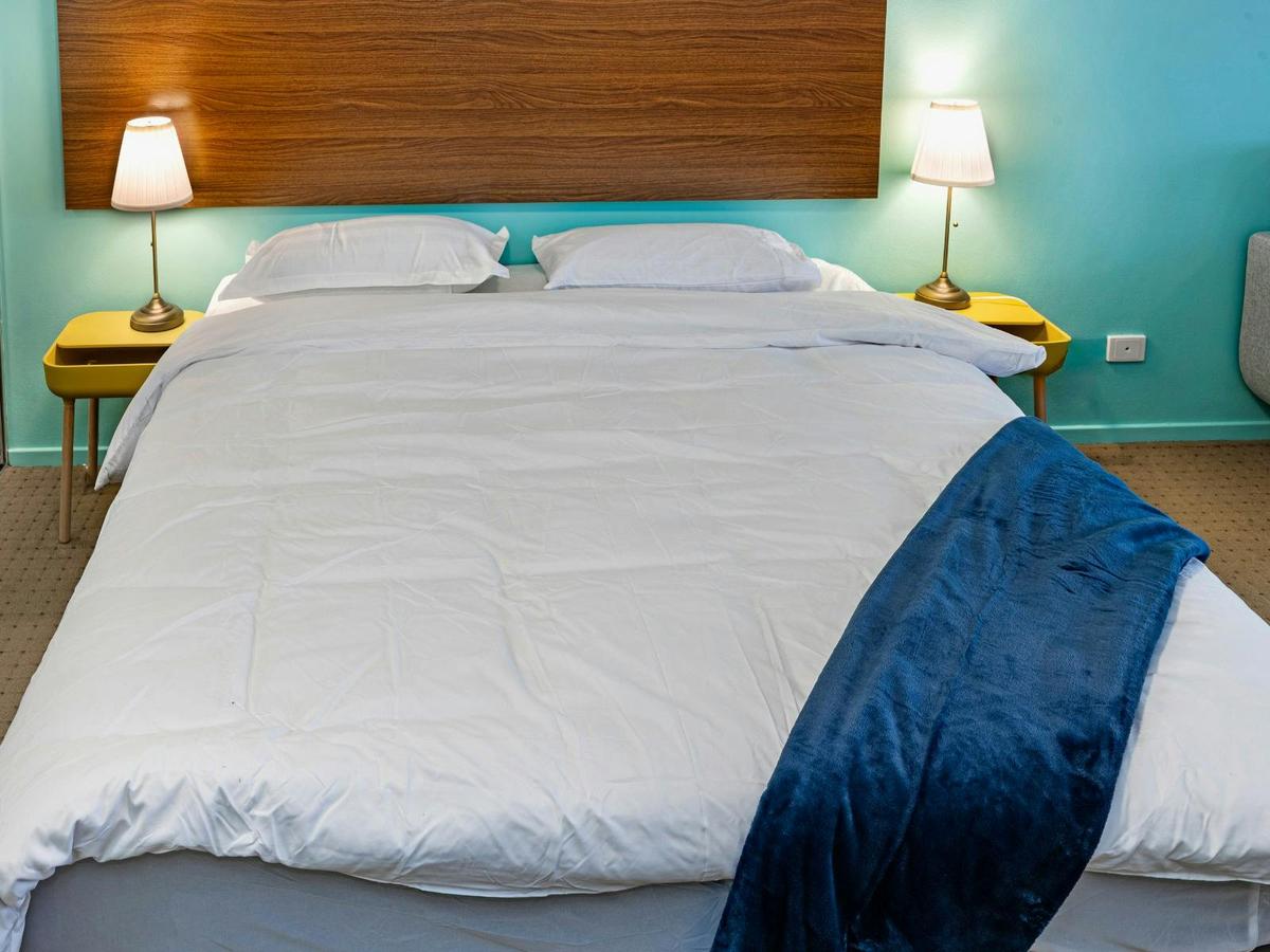 Close-up of the queen-sized bed with bedside lighting and wooden headboard.