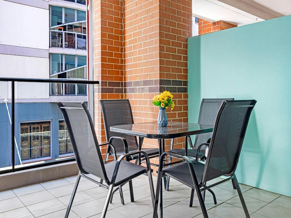 Private balcony with outdoor table and chairs, surrounded by brick and privacy screening.