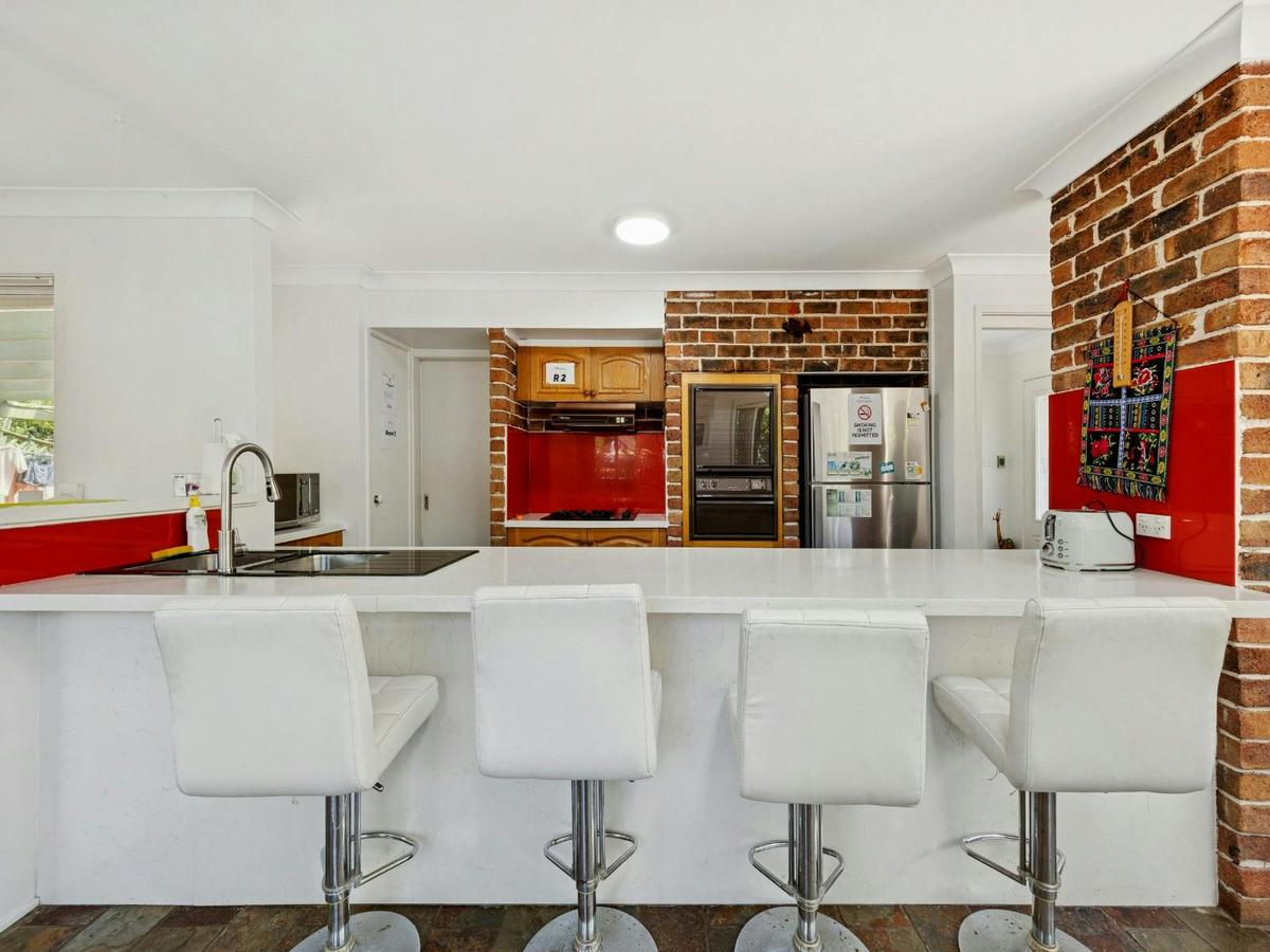 Spacious kitchen with island bench, bar stools, and brick feature wall.